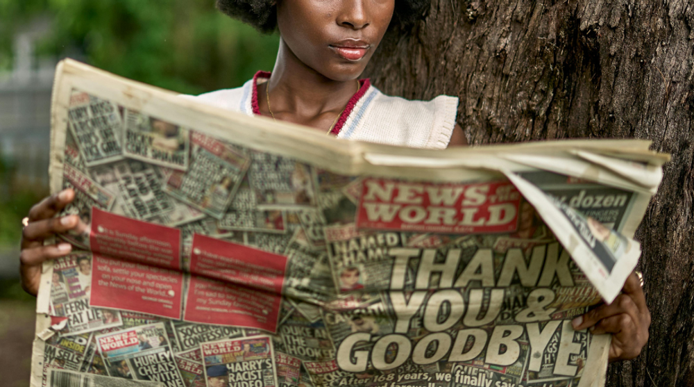 Frau liest die letzte Ausgabe der Boulevardzeitung News of the World mit der Schlagzeile „Thank You & Goodbye“