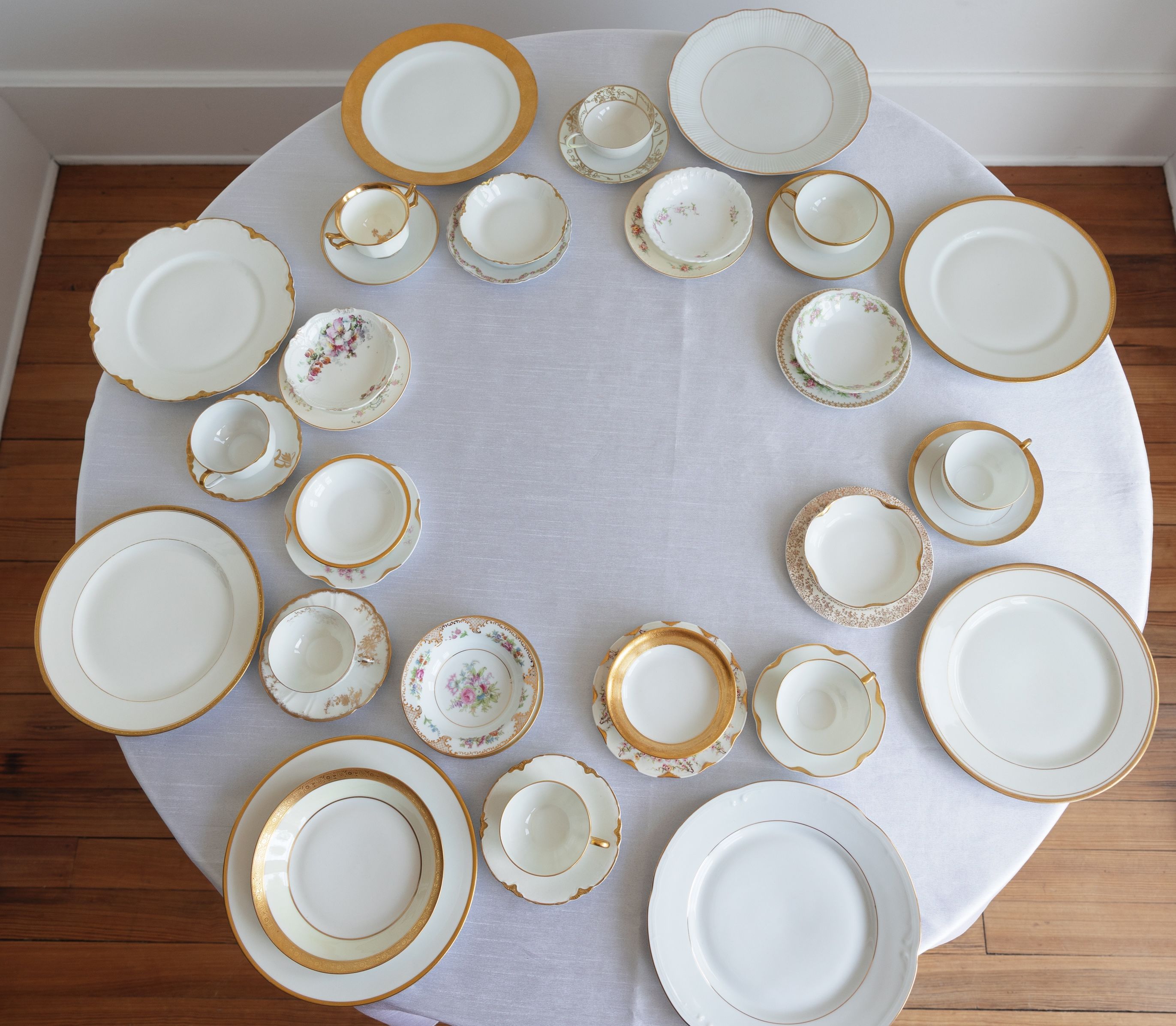 Circular table setting with gold-rimmed china plates and teacups overhead