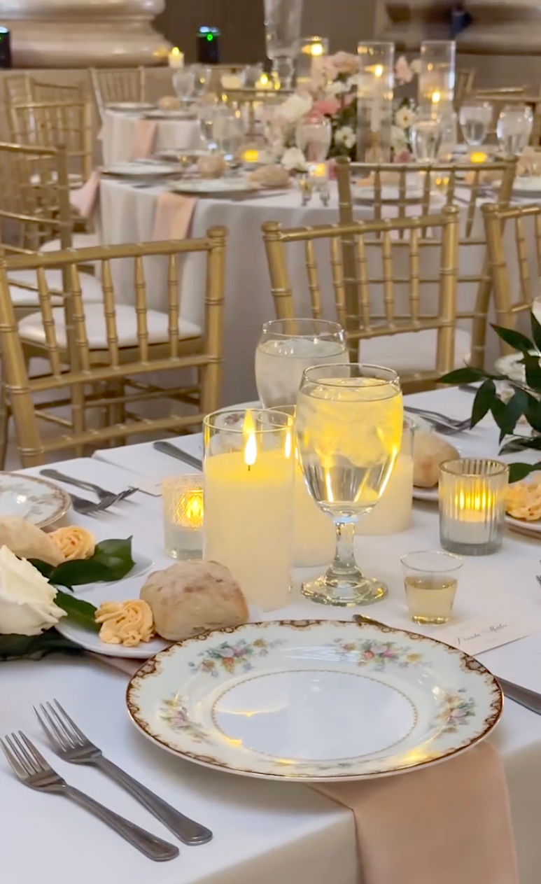 Candlelit ballroom wedding table setting with floral dinnerware and gold chiavari chairs