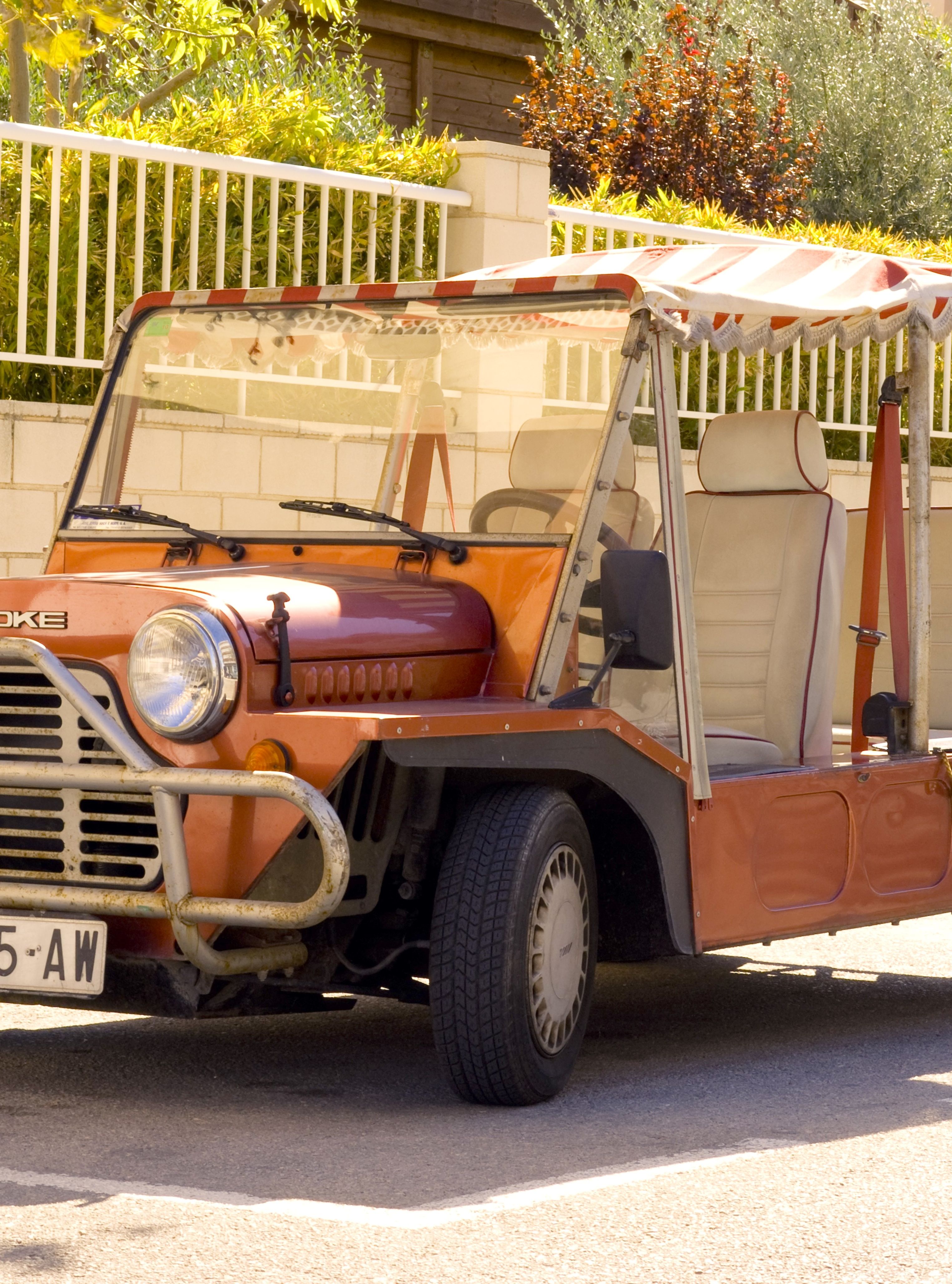 A vintage open-top Moke vehicle parked on a sunny street in a quiet neighborhood