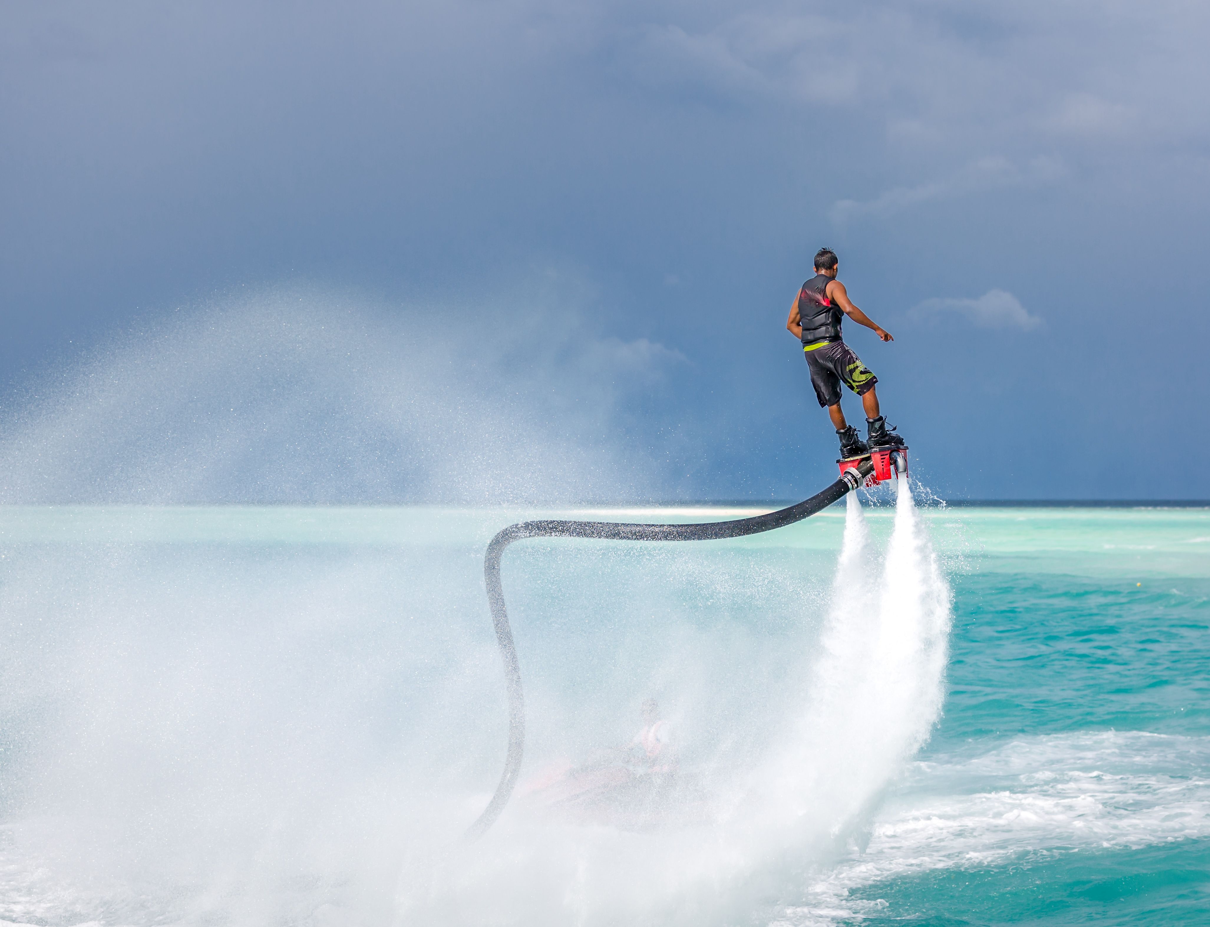 Person performing a water flyboarding stunt, lifted high above the sea with water jets propelling them into the air