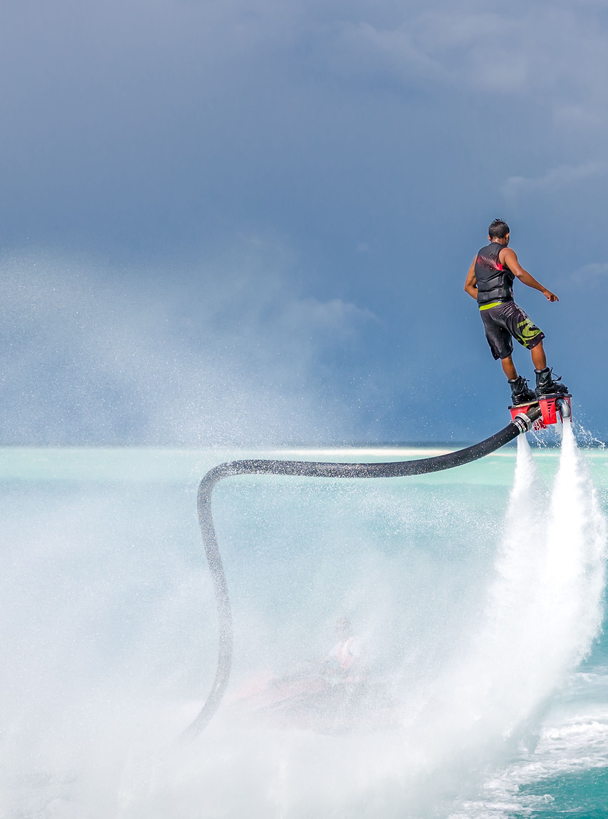 Person performing a water flyboarding stunt, lifted high above the sea with water jets propelling them into the air