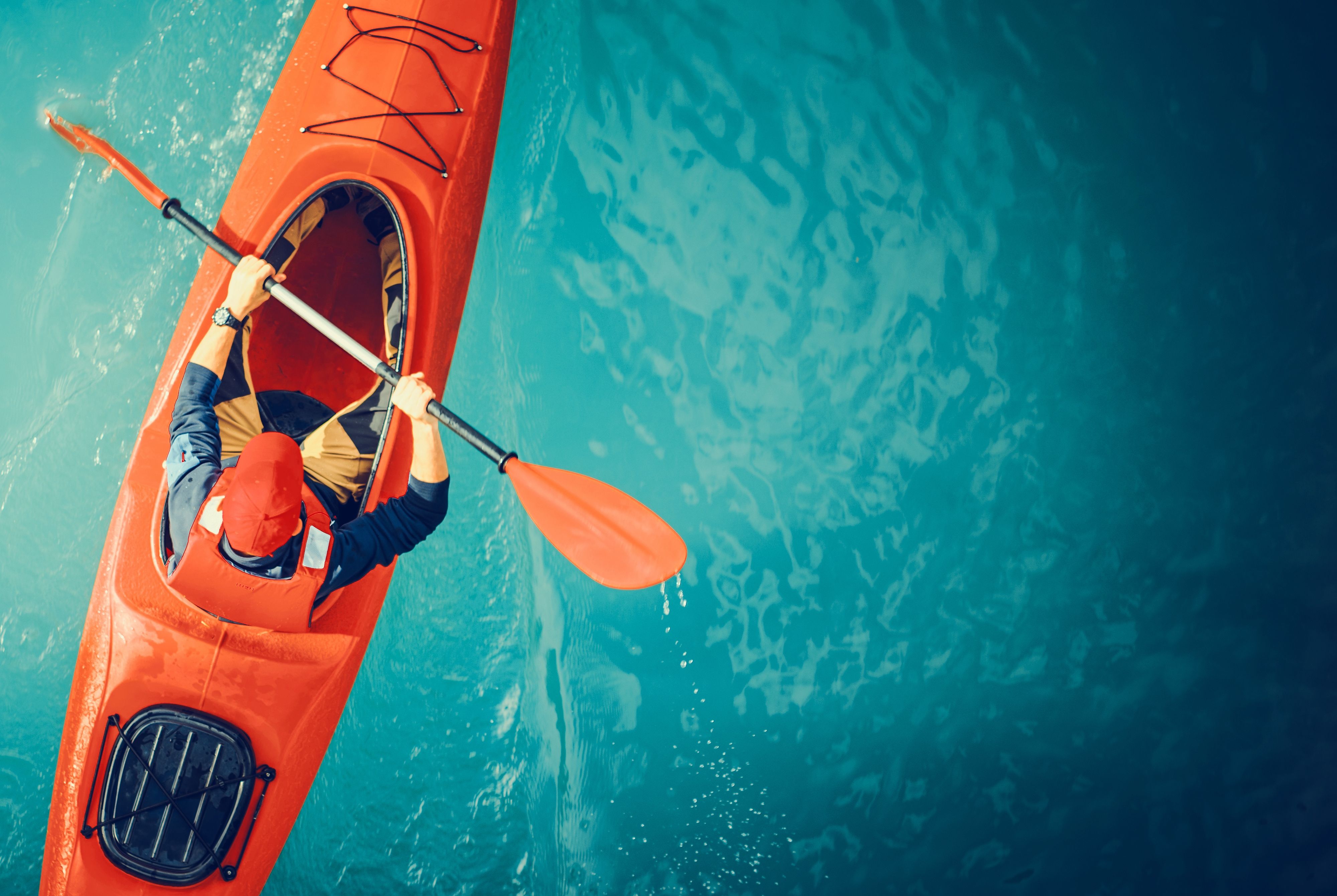 Aerial view of a person kayaking alone in a bright red kayak on a calm blue lake