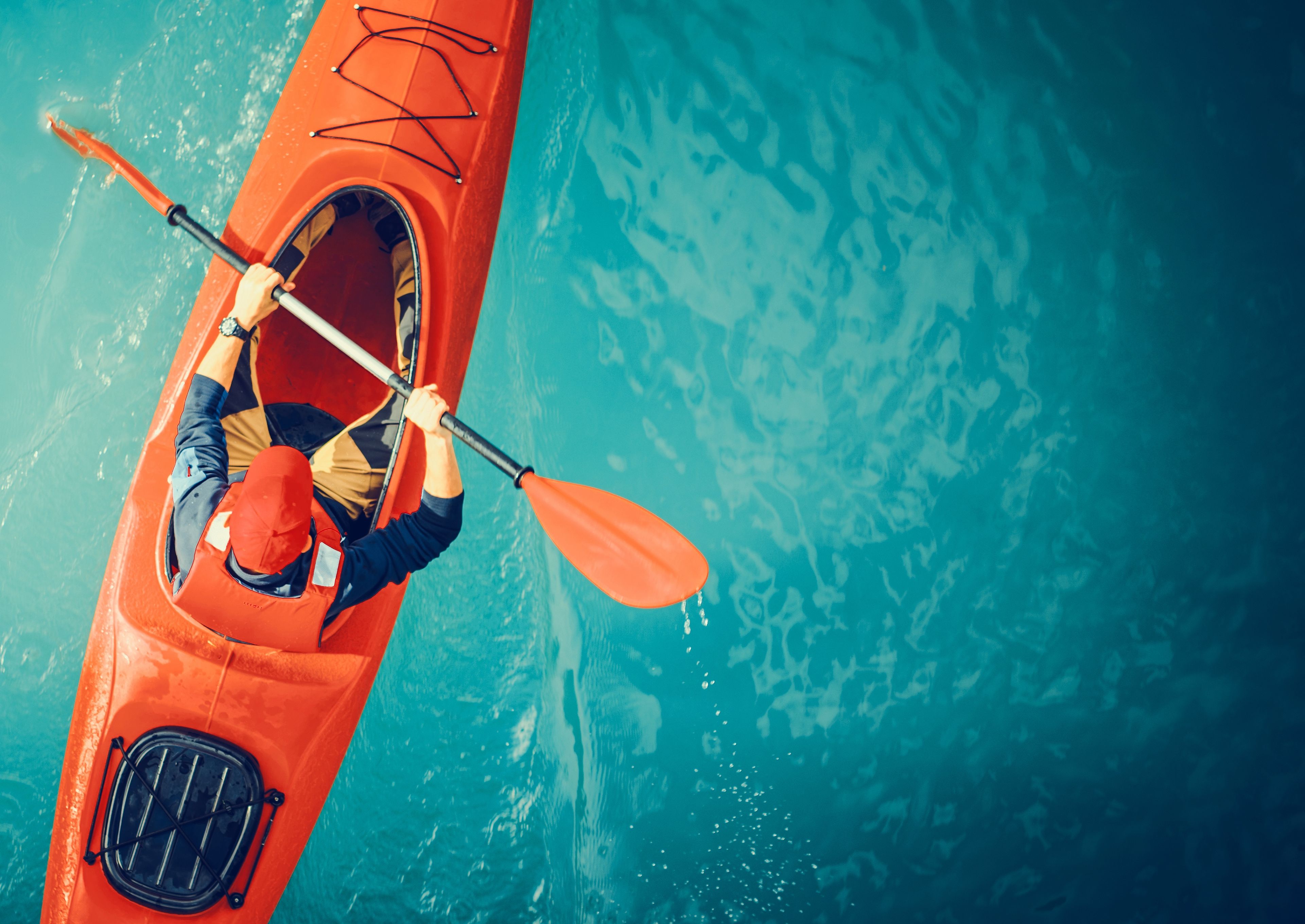 Aerial view of a person kayaking alone in a bright red kayak on a calm blue lake