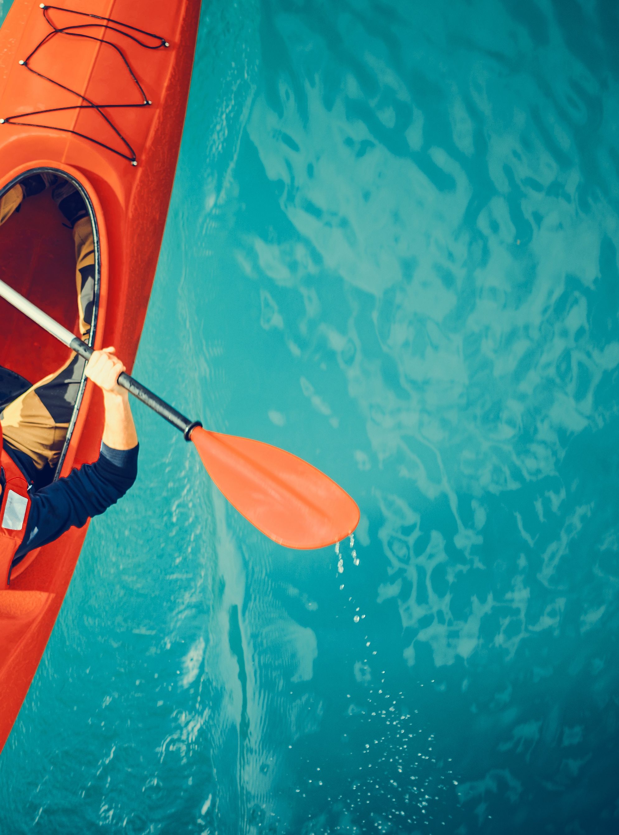 Aerial view of a person kayaking alone in a bright red kayak on a calm blue lake