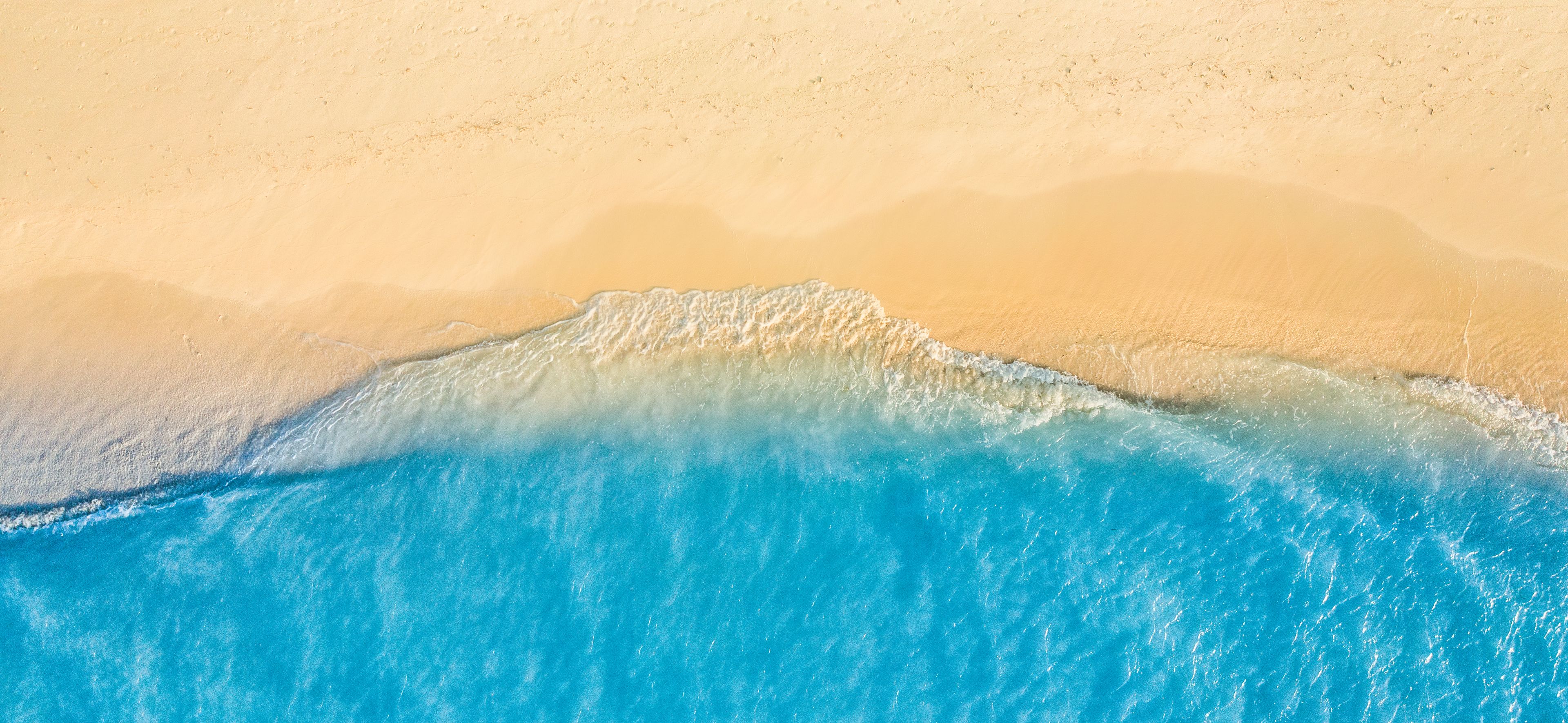 Aerial view of gentle waves washing up on a sandy beach with clear blue water