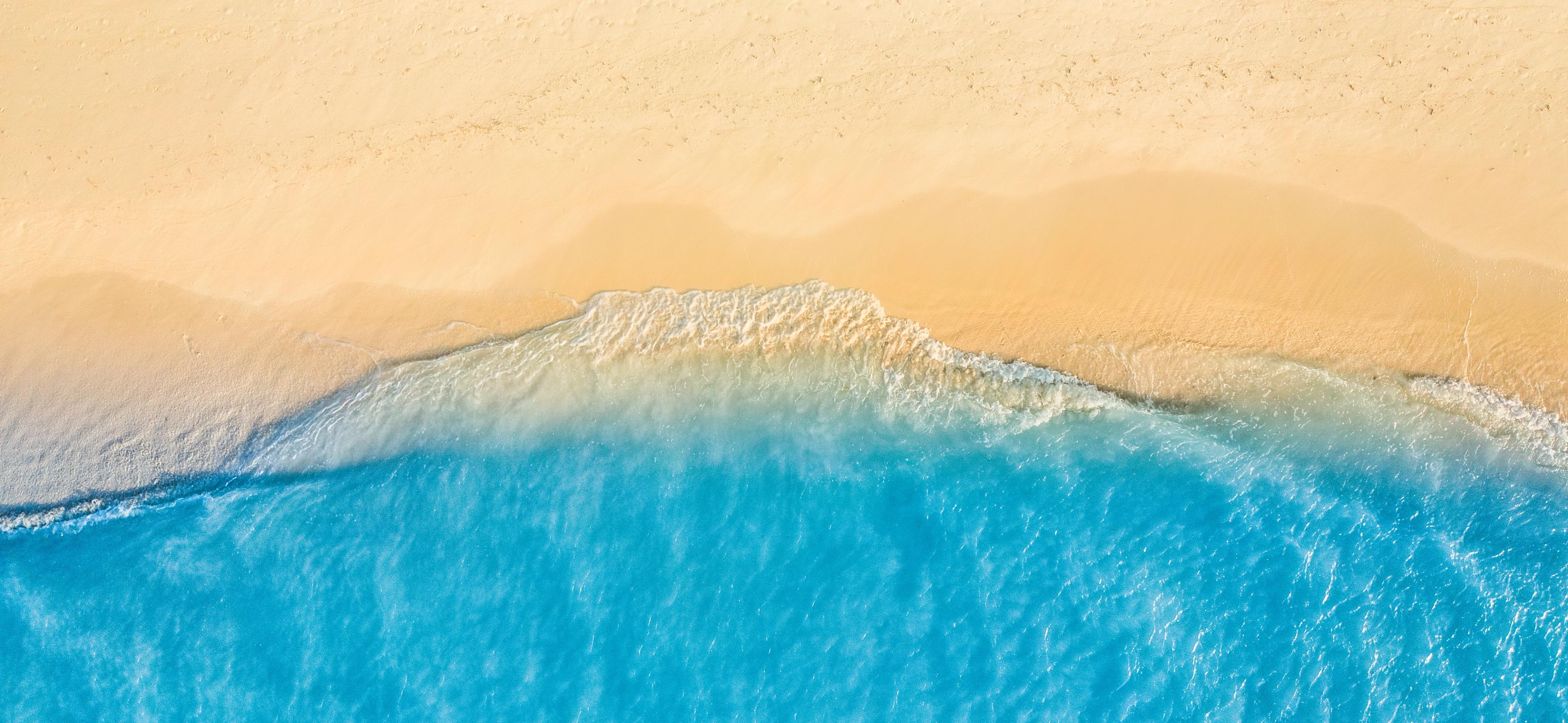 Aerial view of gentle waves washing up on a sandy beach with clear blue water