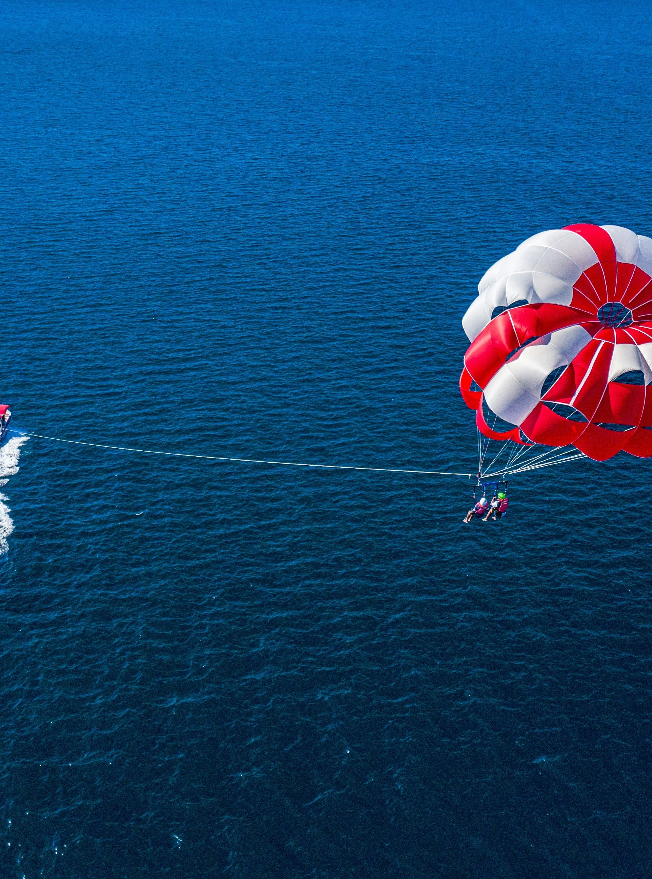 Aerial view of a boat pulling a person parasailing high above the open ocean under a large red and white parachute