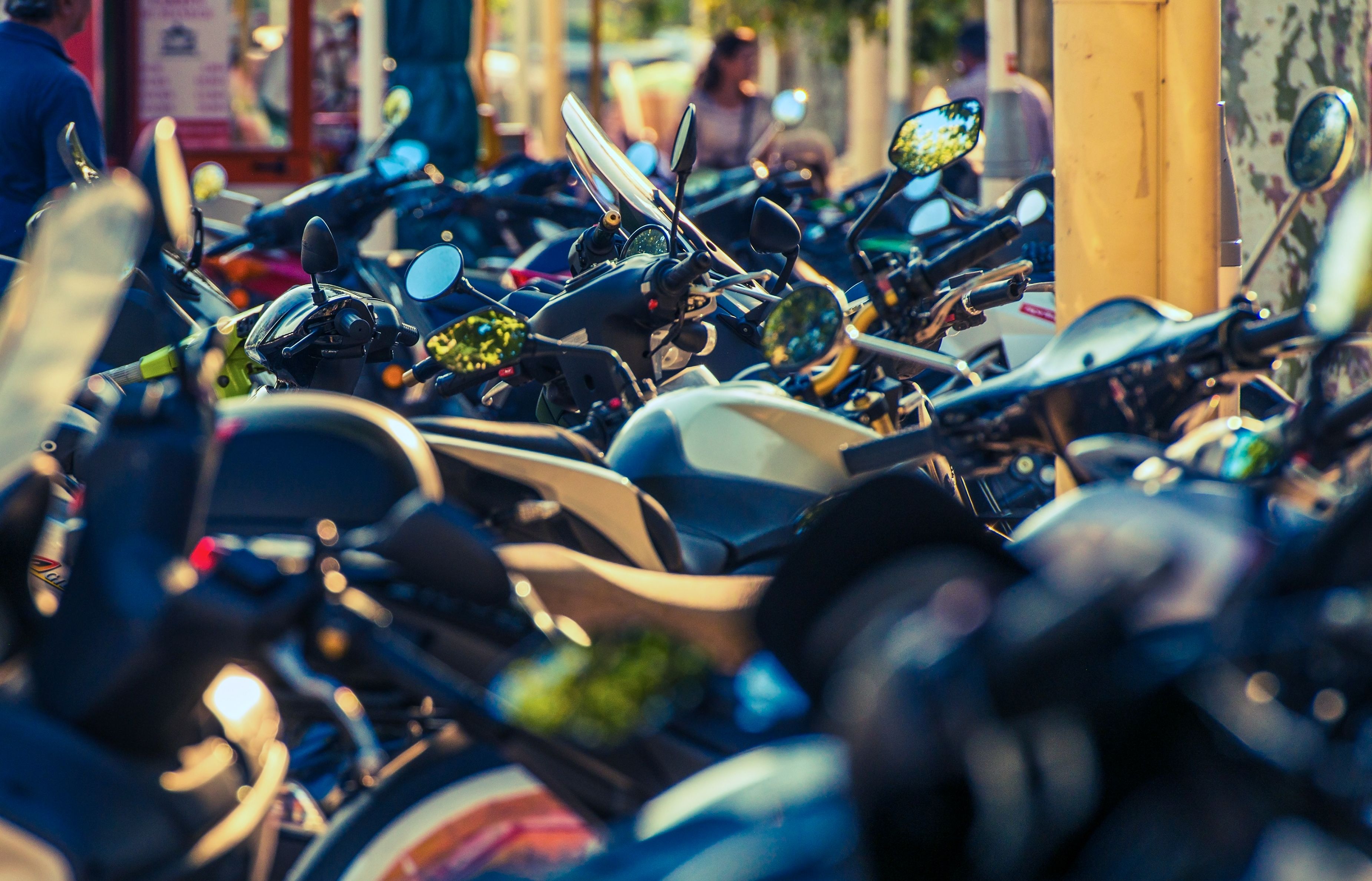 Row of parked motorcycles along a busy street with people walking in the background, capturing the vibrant city atmosphere