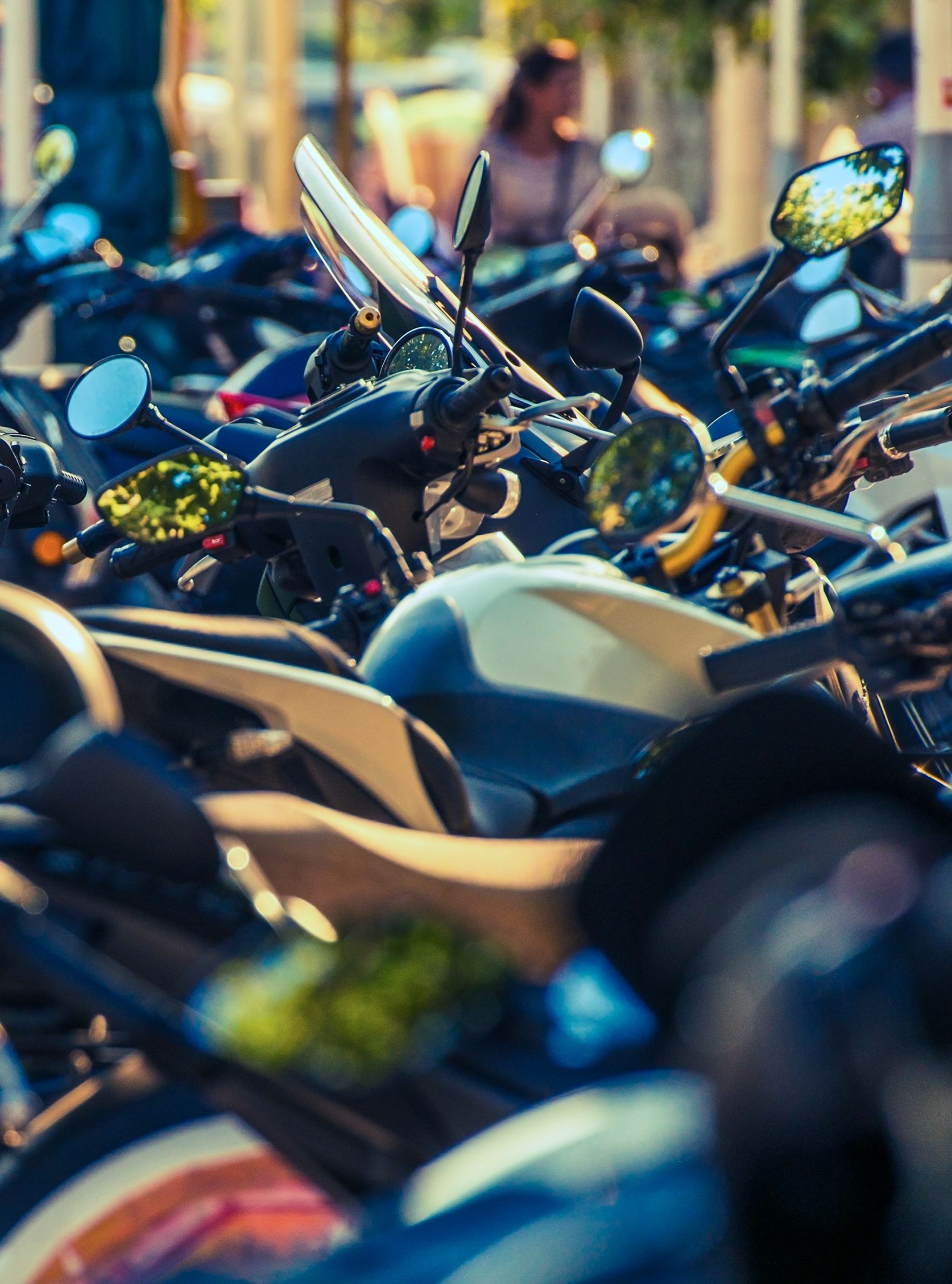 Row of parked motorcycles along a busy street with people walking in the background, capturing the vibrant city atmosphere