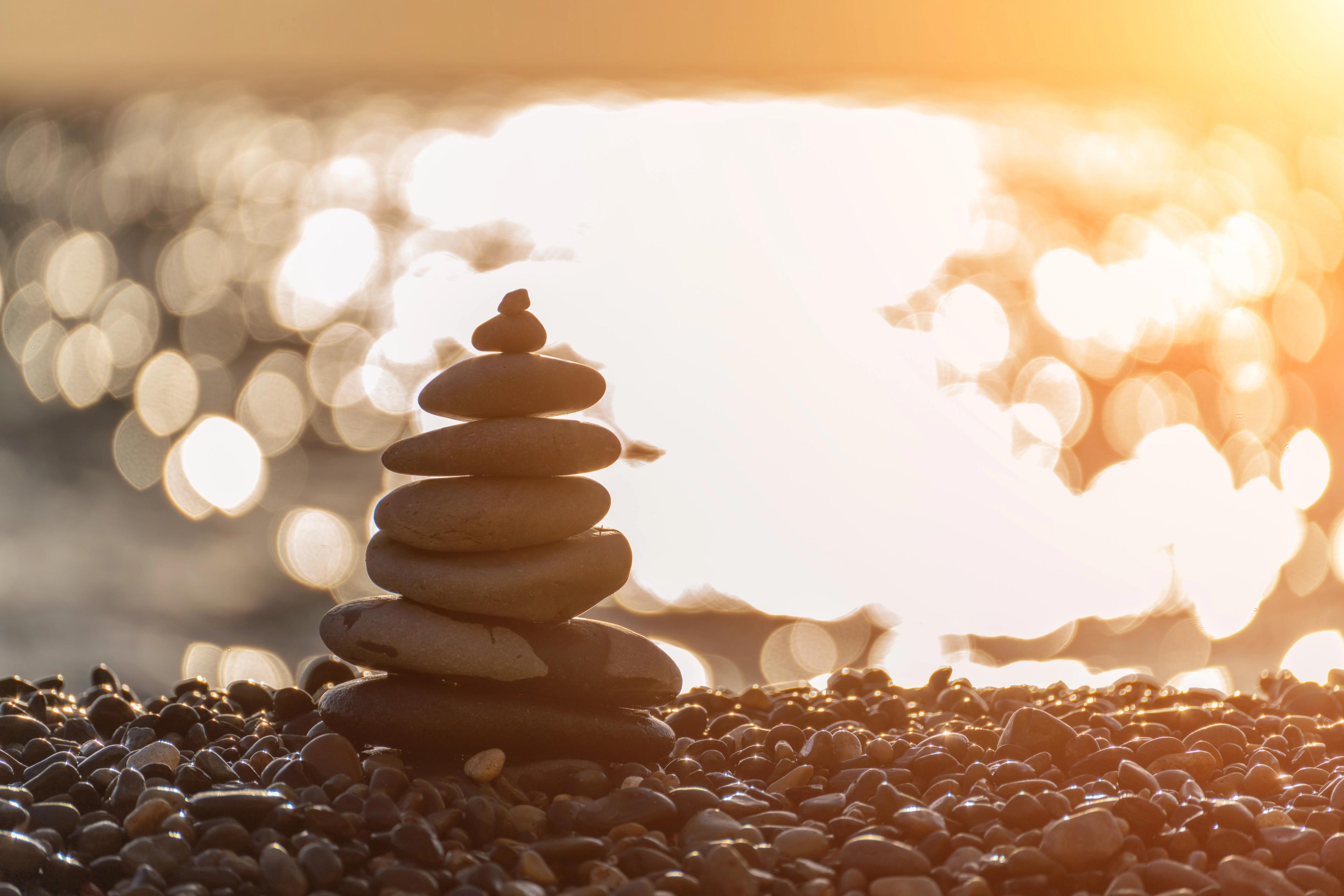 Stack of pebbles on a beach, symbolizing tranquility, with a sunset reflecting on the water