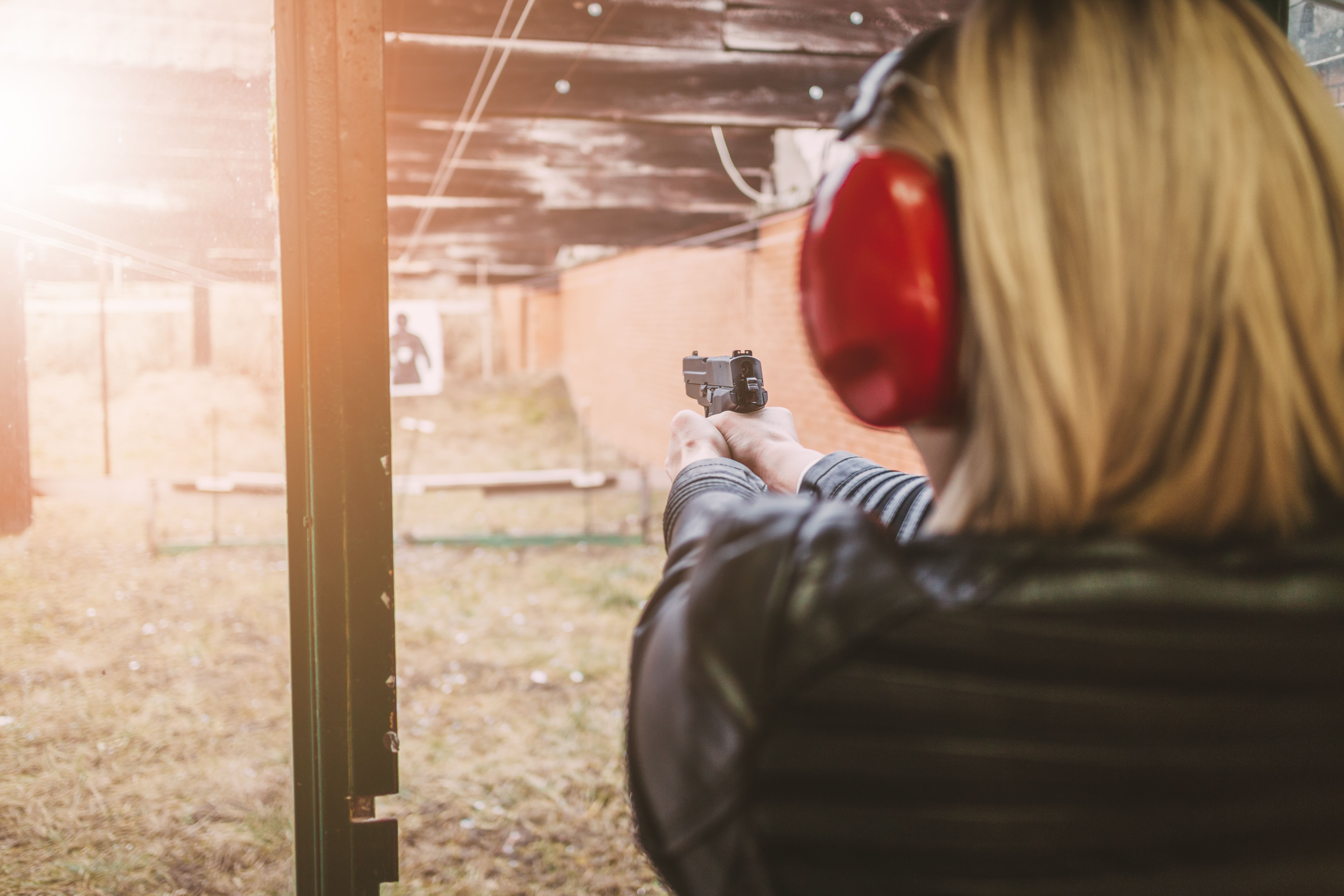 Woman at a shooting range wearing protective headphones, aiming a handgun at a target in the distance