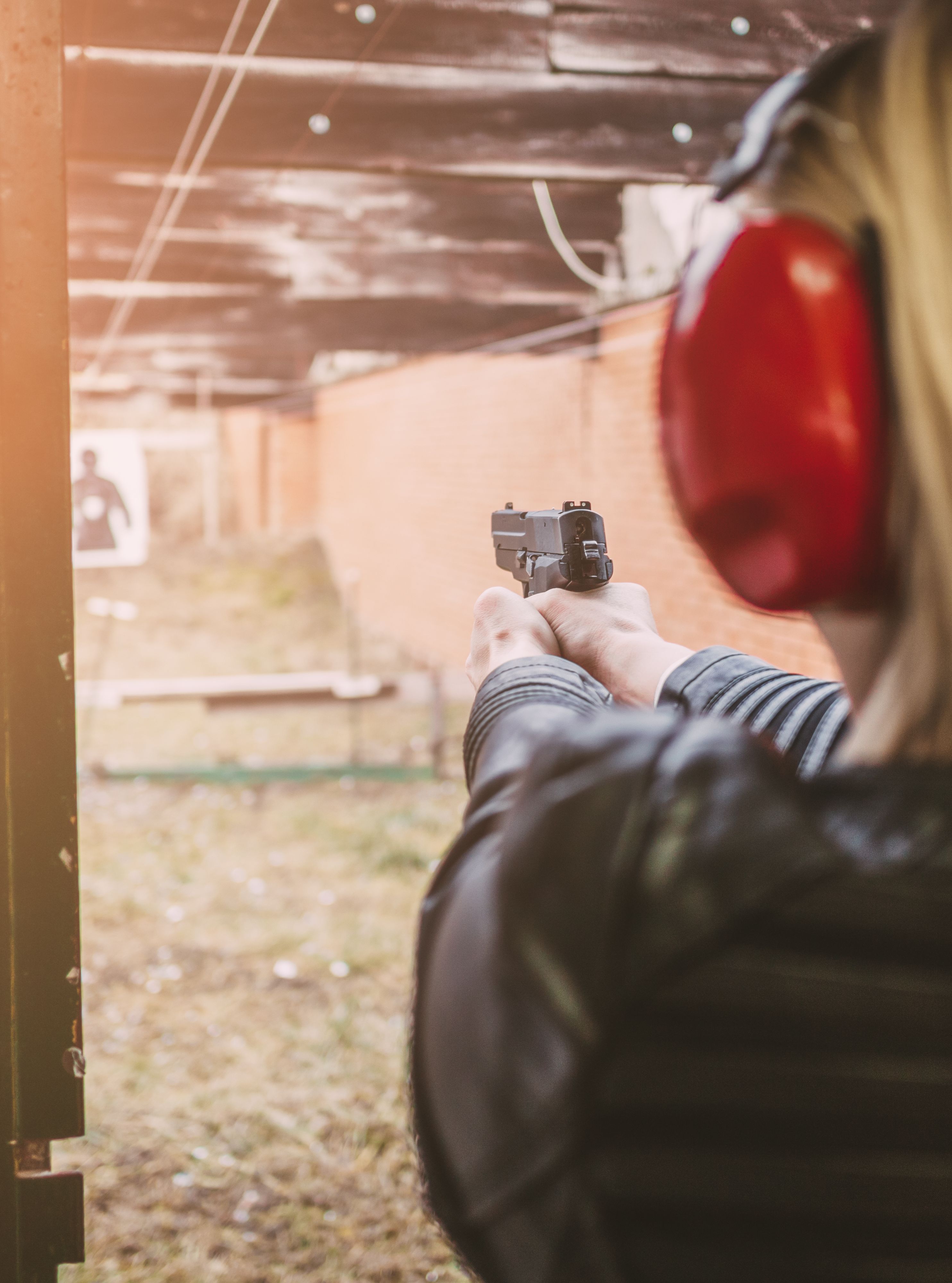 Woman at a shooting range wearing protective headphones, aiming a handgun at a target in the distance