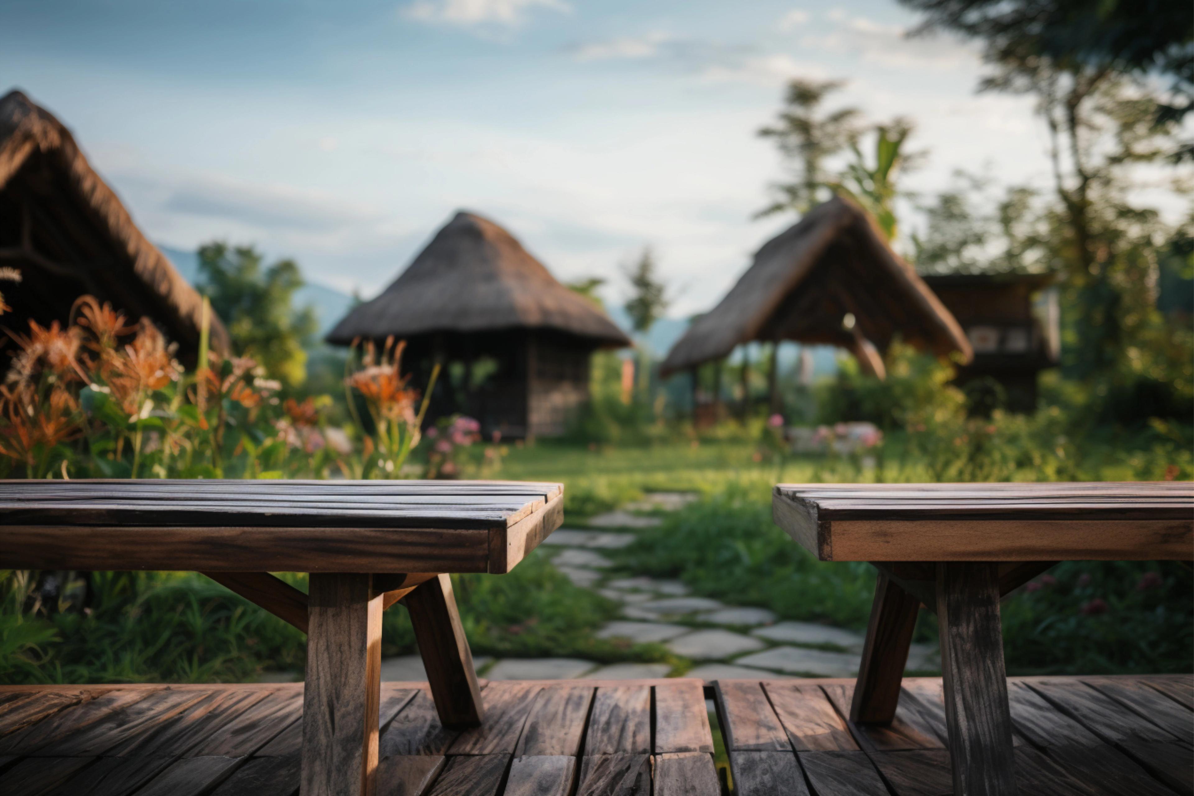 Wooden benches on a deck overlooking a lush garden with thatched huts in the background, capturing a peaceful rural setting