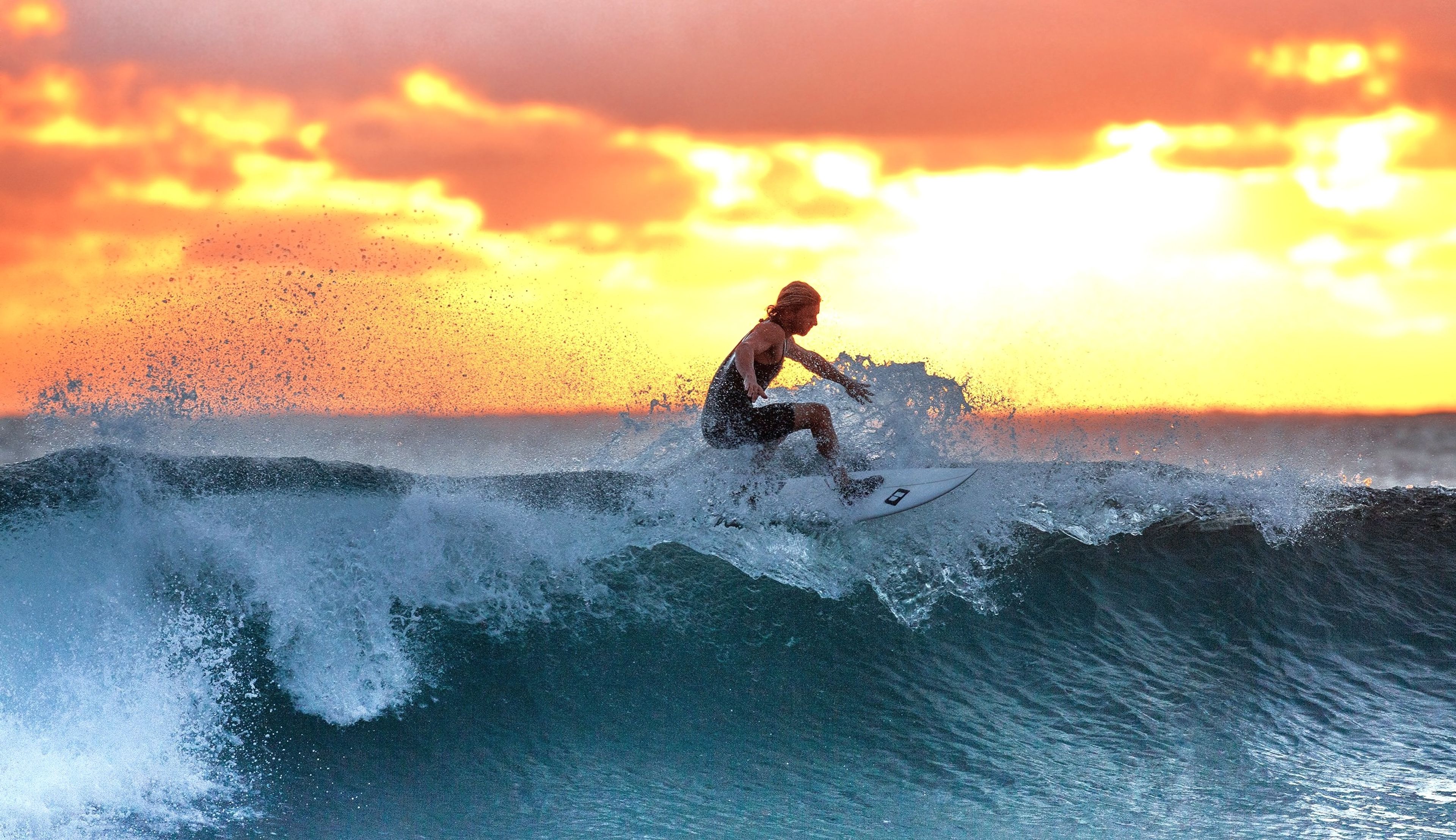 Surfer catching a wave during a vibrant orange sunset, with waves crashing beneath the board