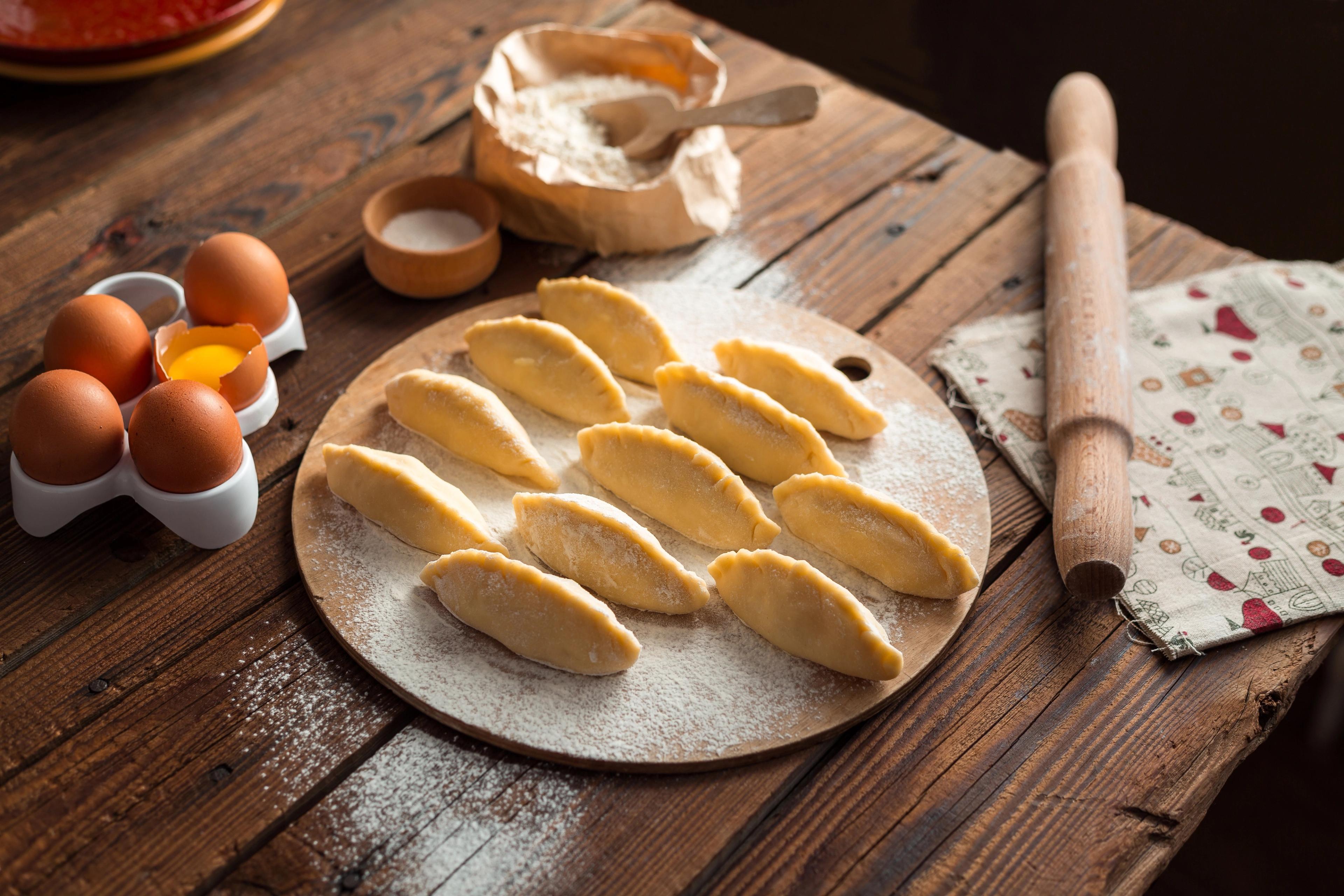 Freshly made dumplings arranged on a wooden board, ready for cooking, with ingredients and tools on the table