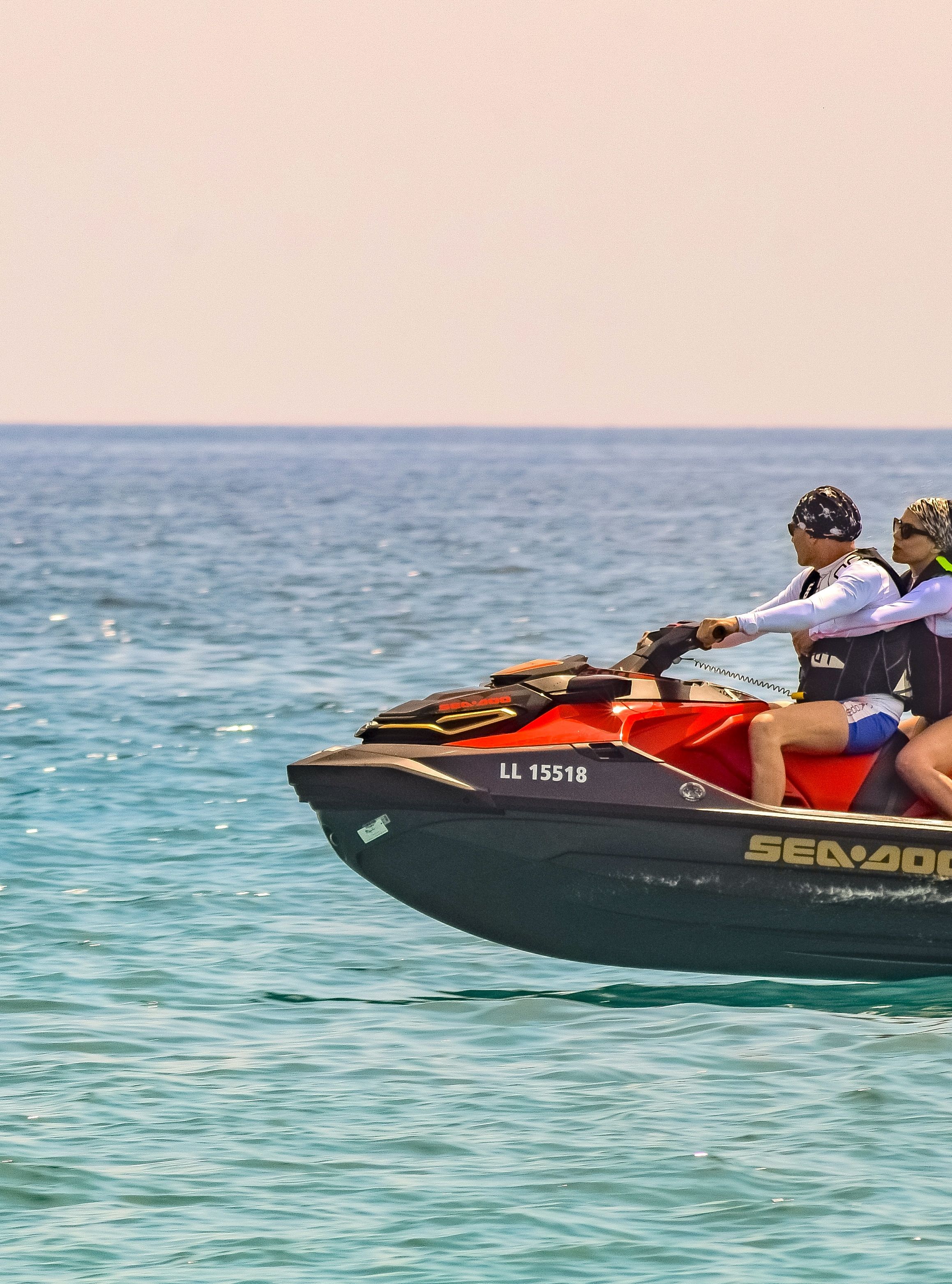 Two people riding a red jet ski across the ocean on a bright sunny day, leaving a trail of water behind