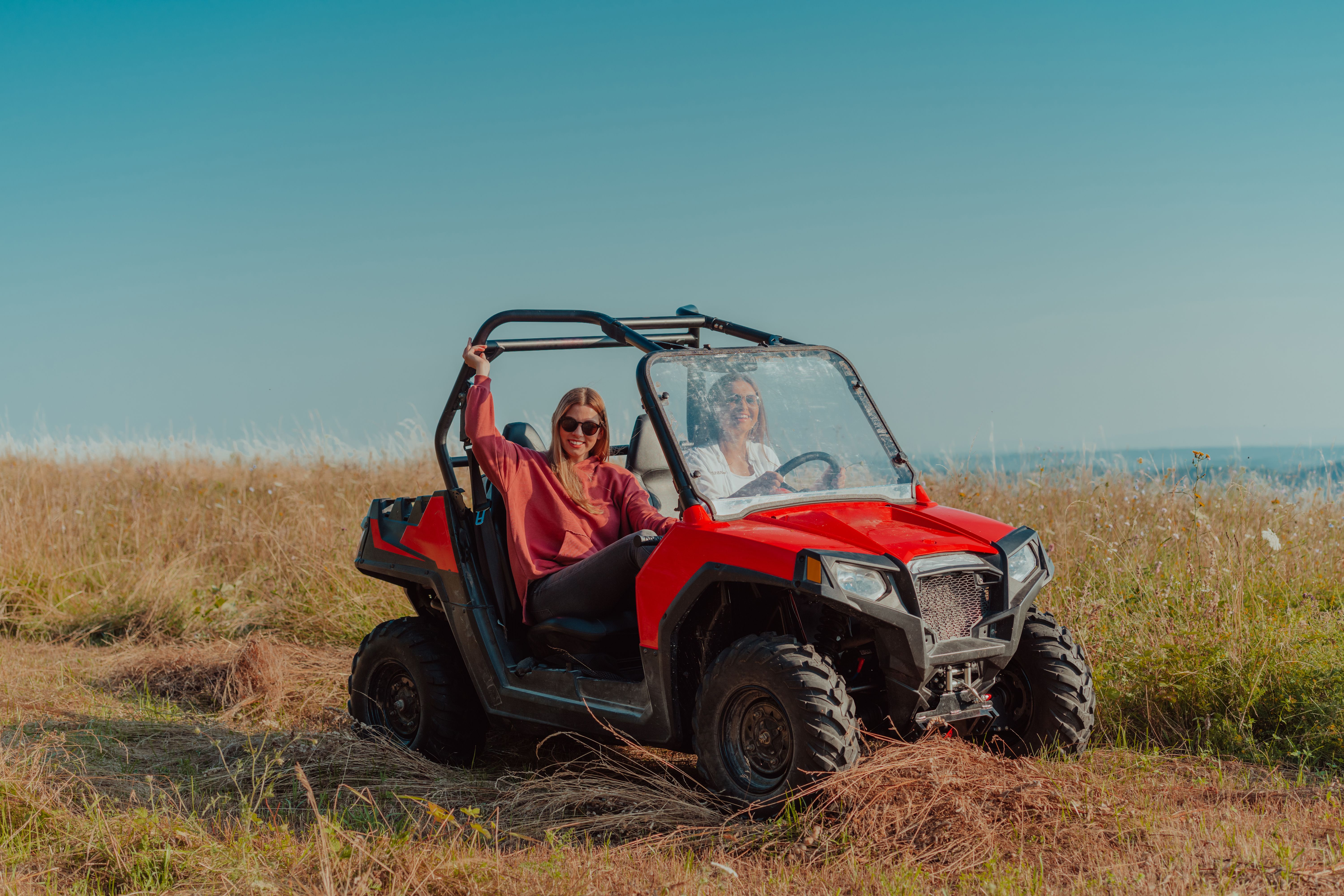 Two women smiling and riding a buggy in an open grassy field under a clear sky