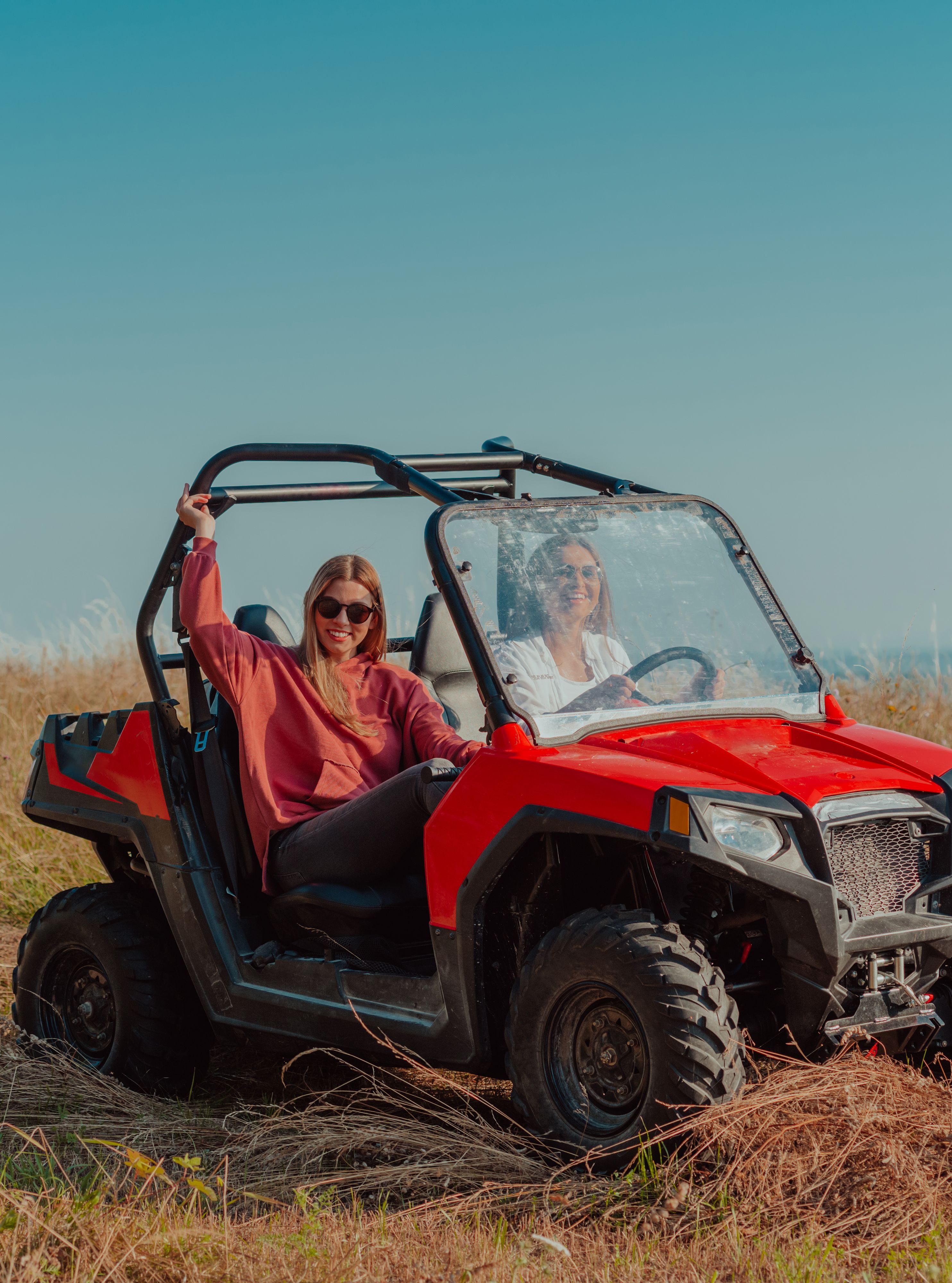 Two women smiling and riding a buggy in an open grassy field under a clear sky
