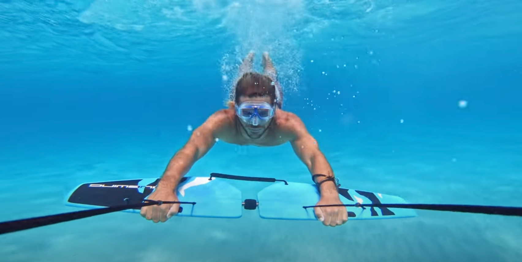 Person snorkeling underwater, holding onto a subwing board and gliding through clear blue water