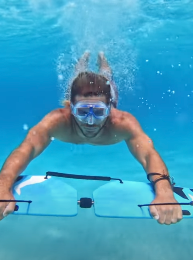 Person snorkeling underwater, holding onto a subwing board and gliding through clear blue water