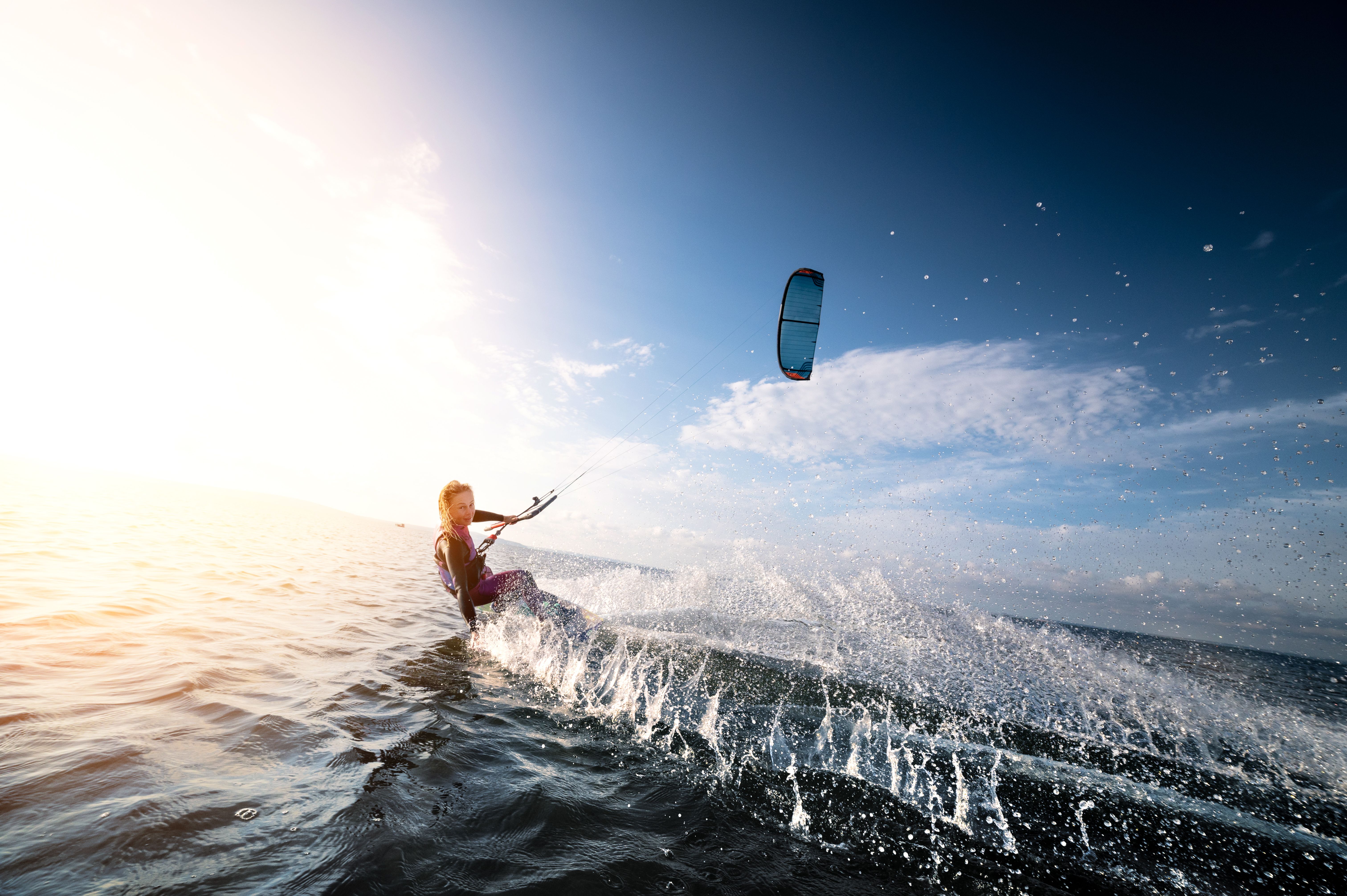 Kitesurfer riding the waves with a colorful kite above, during a beautiful sunny day over the sea