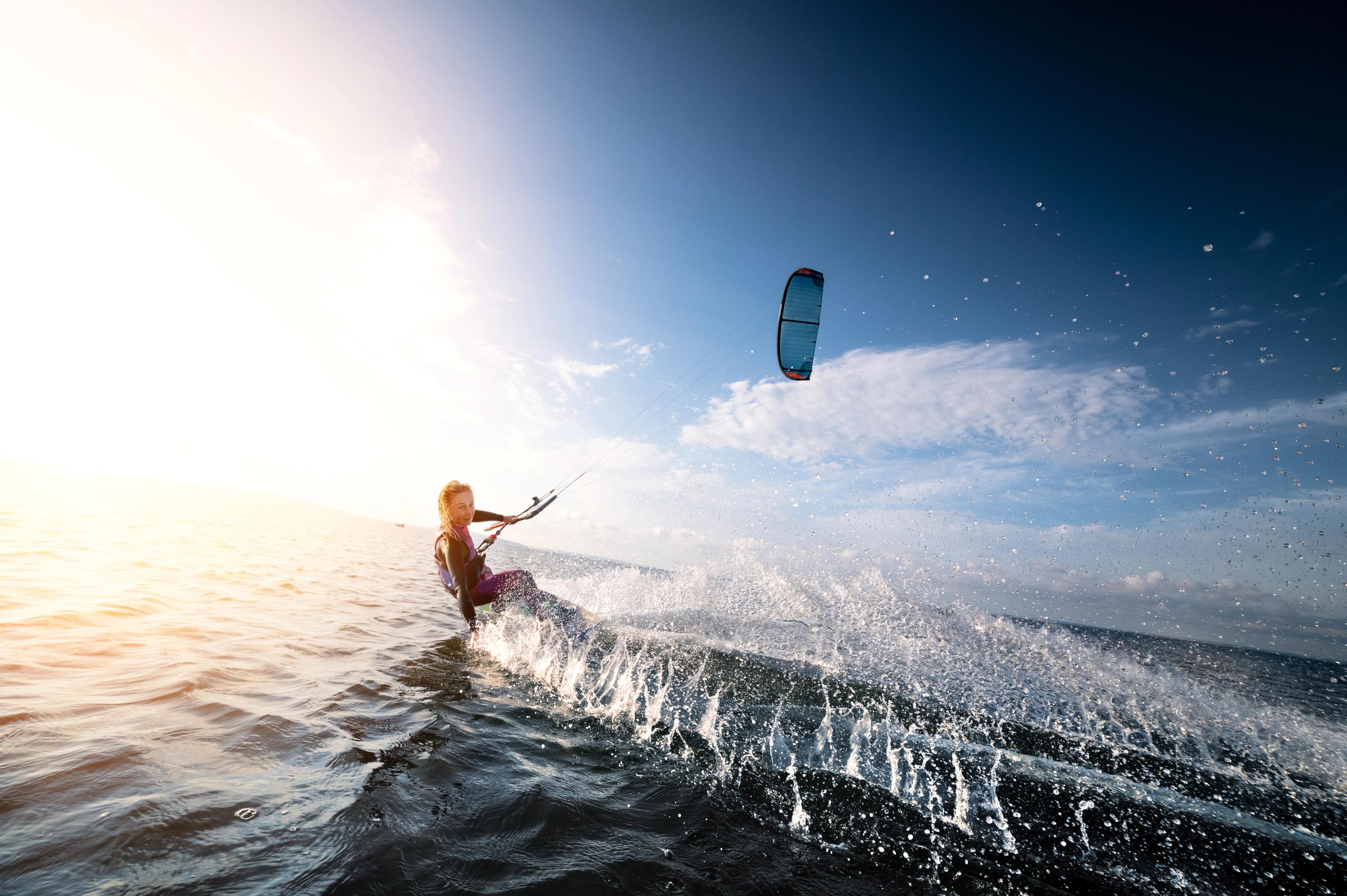 Kitesurfer riding the waves with a colorful kite above, during a beautiful sunny day over the sea