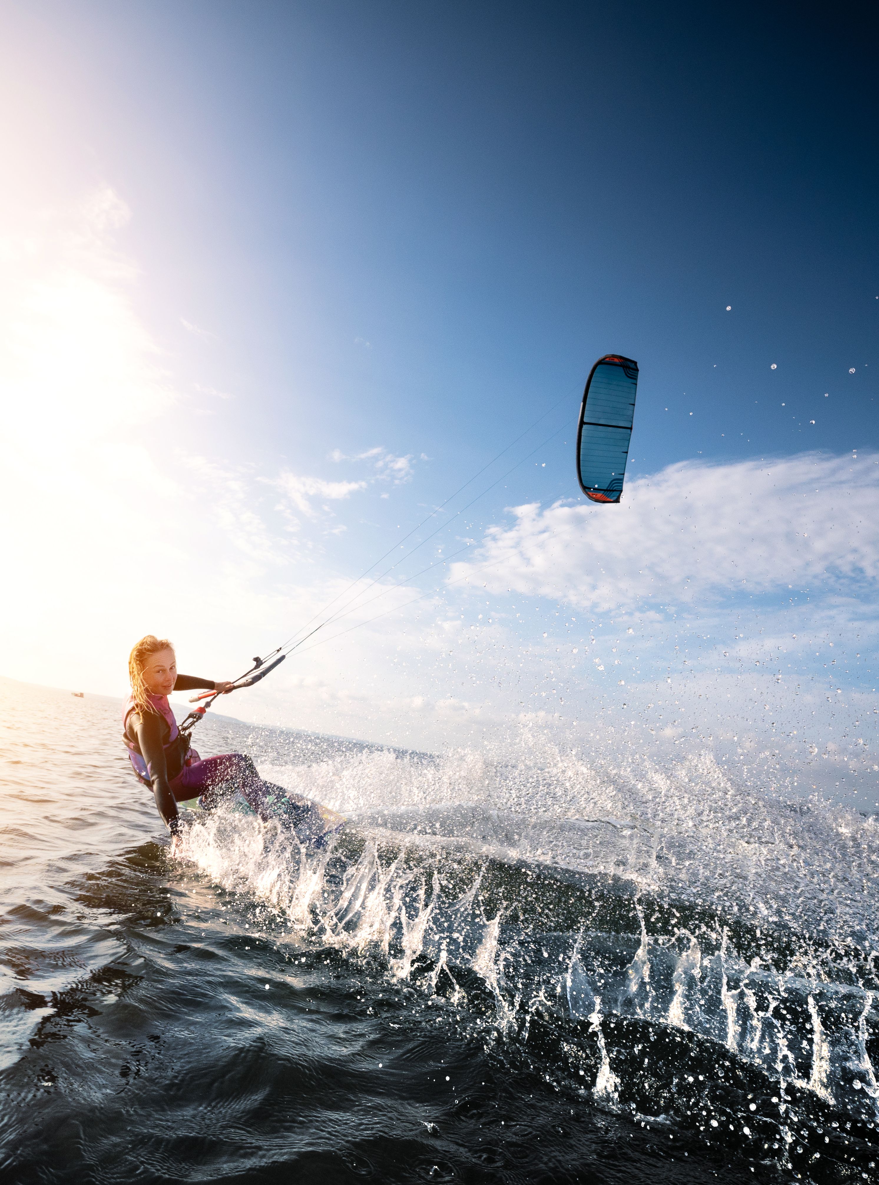 Kitesurfer riding the waves with a colorful kite above, during a beautiful sunny day over the sea