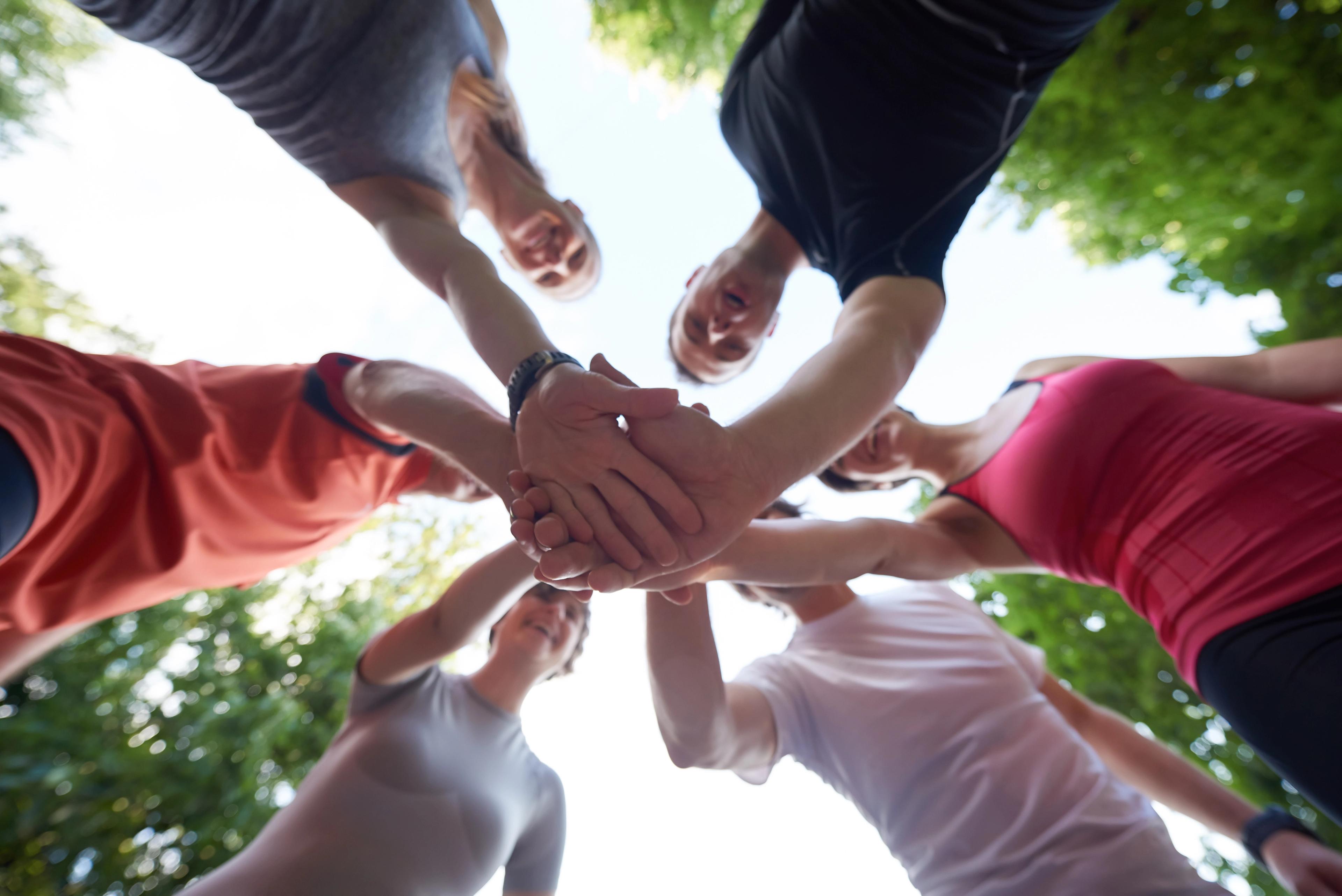 Group of people standing in a circle with their hands stacked together, symbolizing unity and teamwork