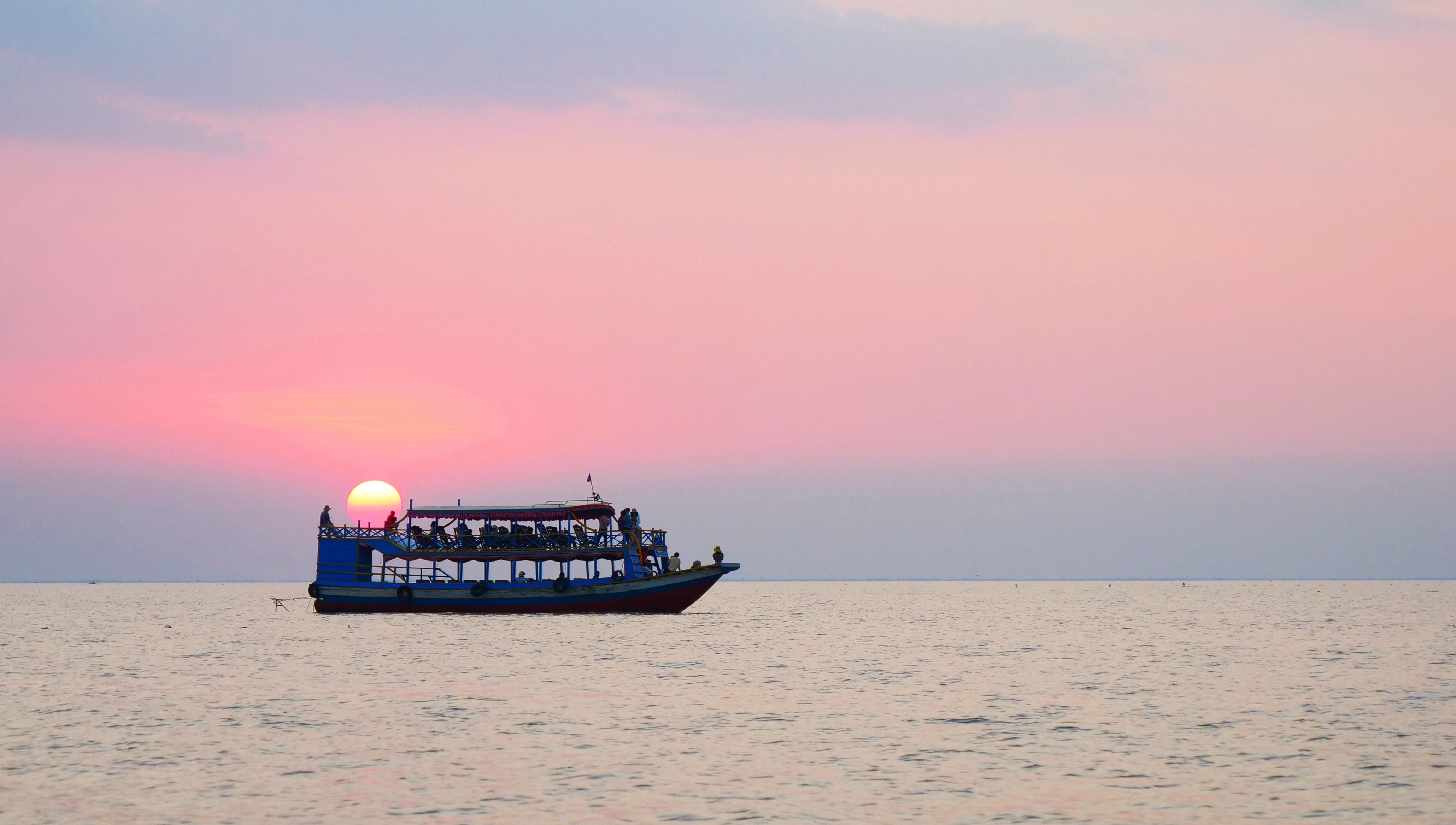 A boat sailing on calm water during a beautiful pink sunset, with the sun just above the horizon