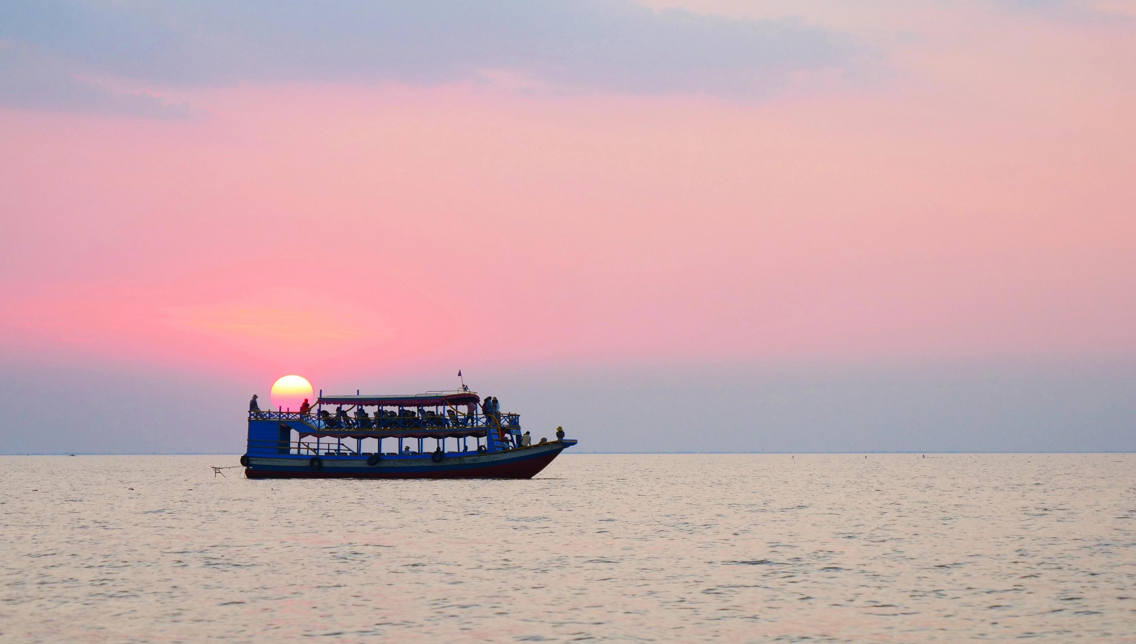A boat sailing on calm water during a beautiful pink sunset, with the sun just above the horizon