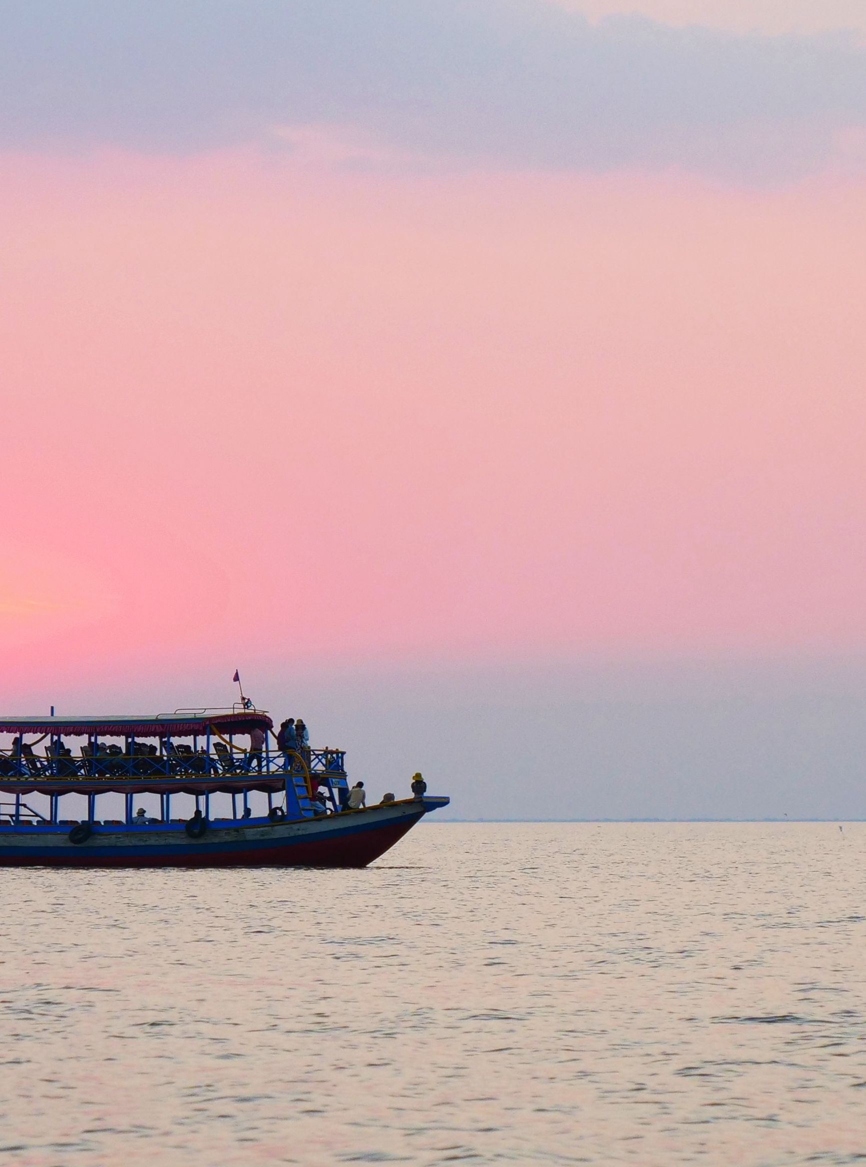 A boat sailing on calm water during a beautiful pink sunset, with the sun just above the horizon