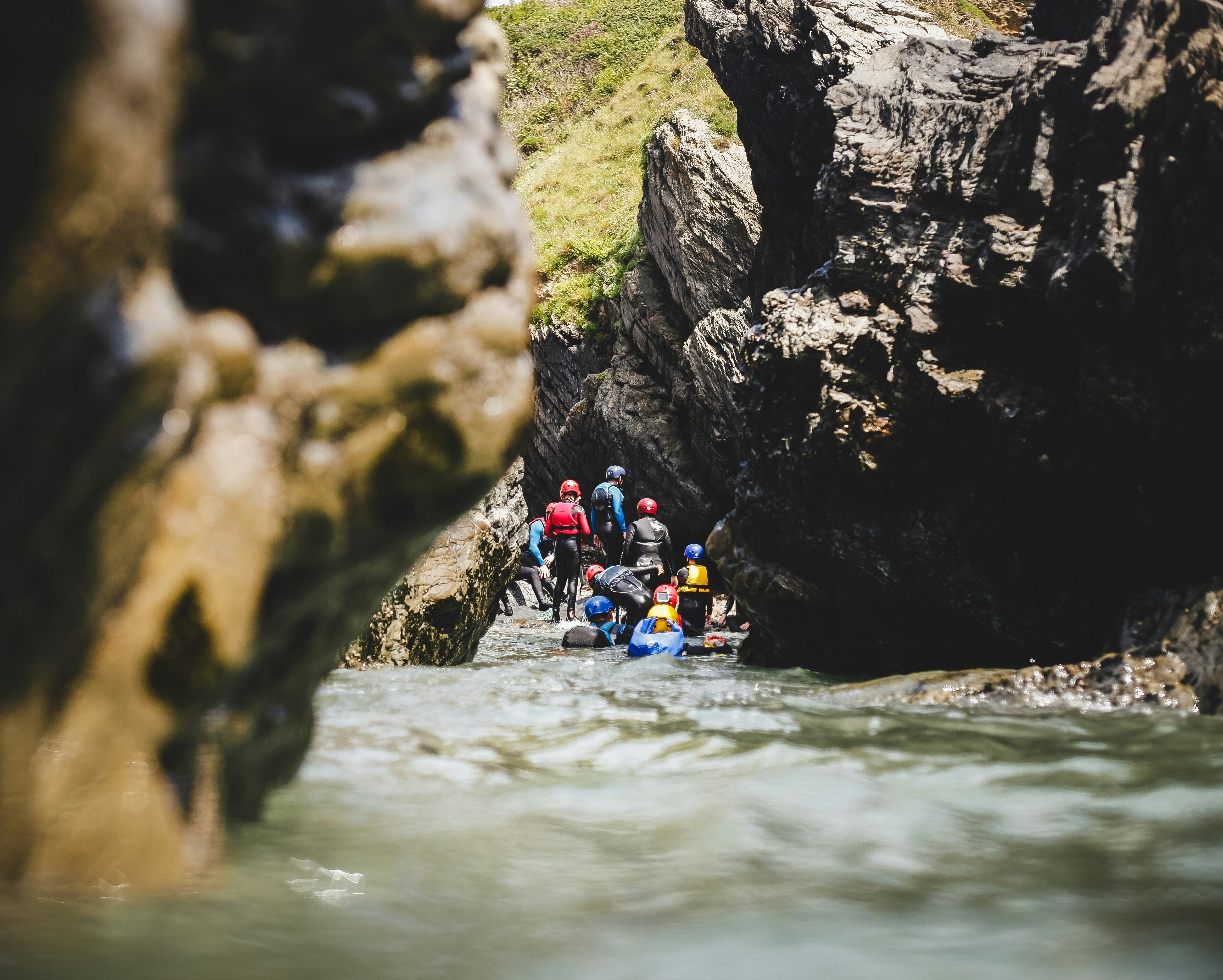 Group of people in wetsuits exploring a narrow rocky canyon while coasteering through a river