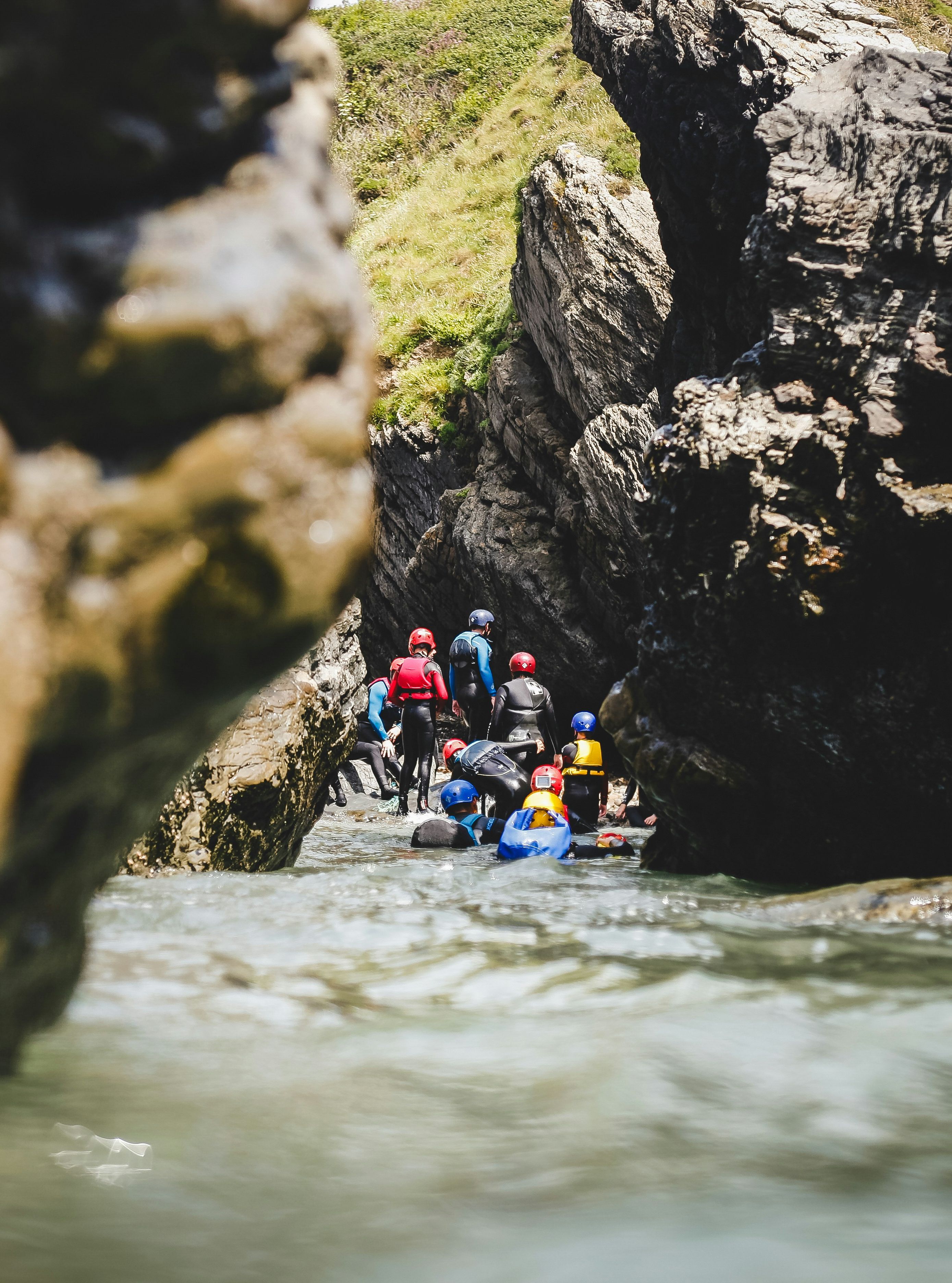 Group of people in wetsuits exploring a narrow rocky canyon while coasteering through a river