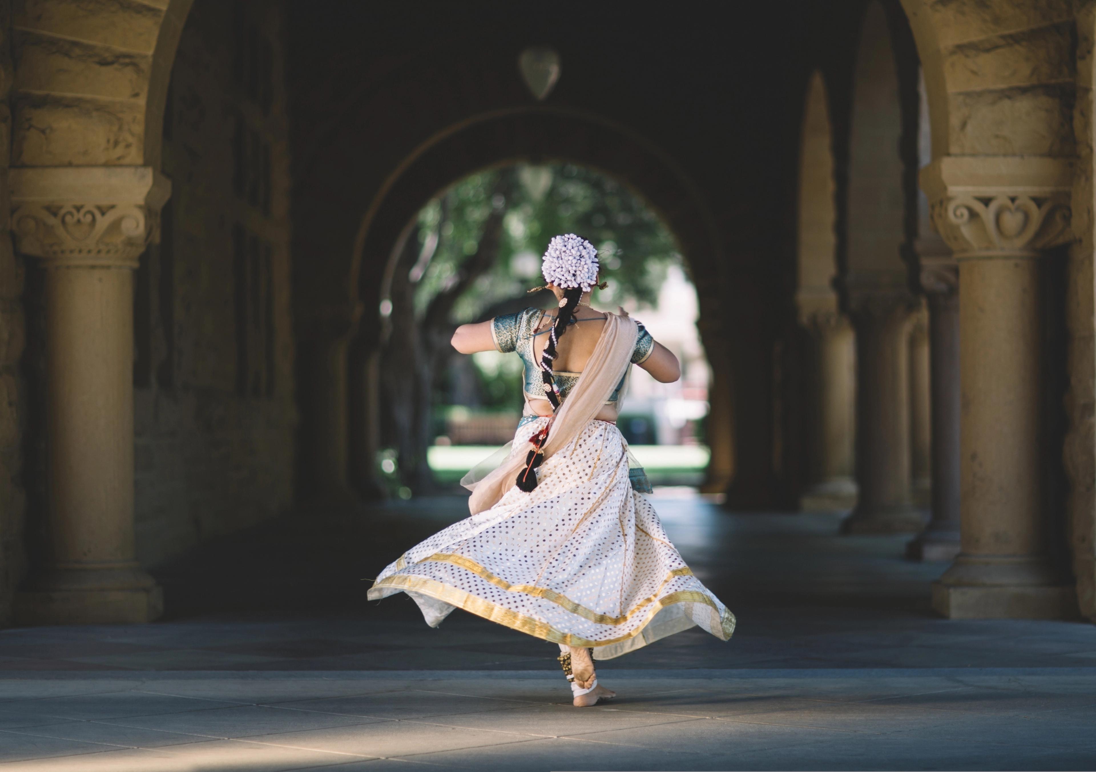 A woman twirling in a traditional white dress in a courtyard with arched columns, captured in motion
