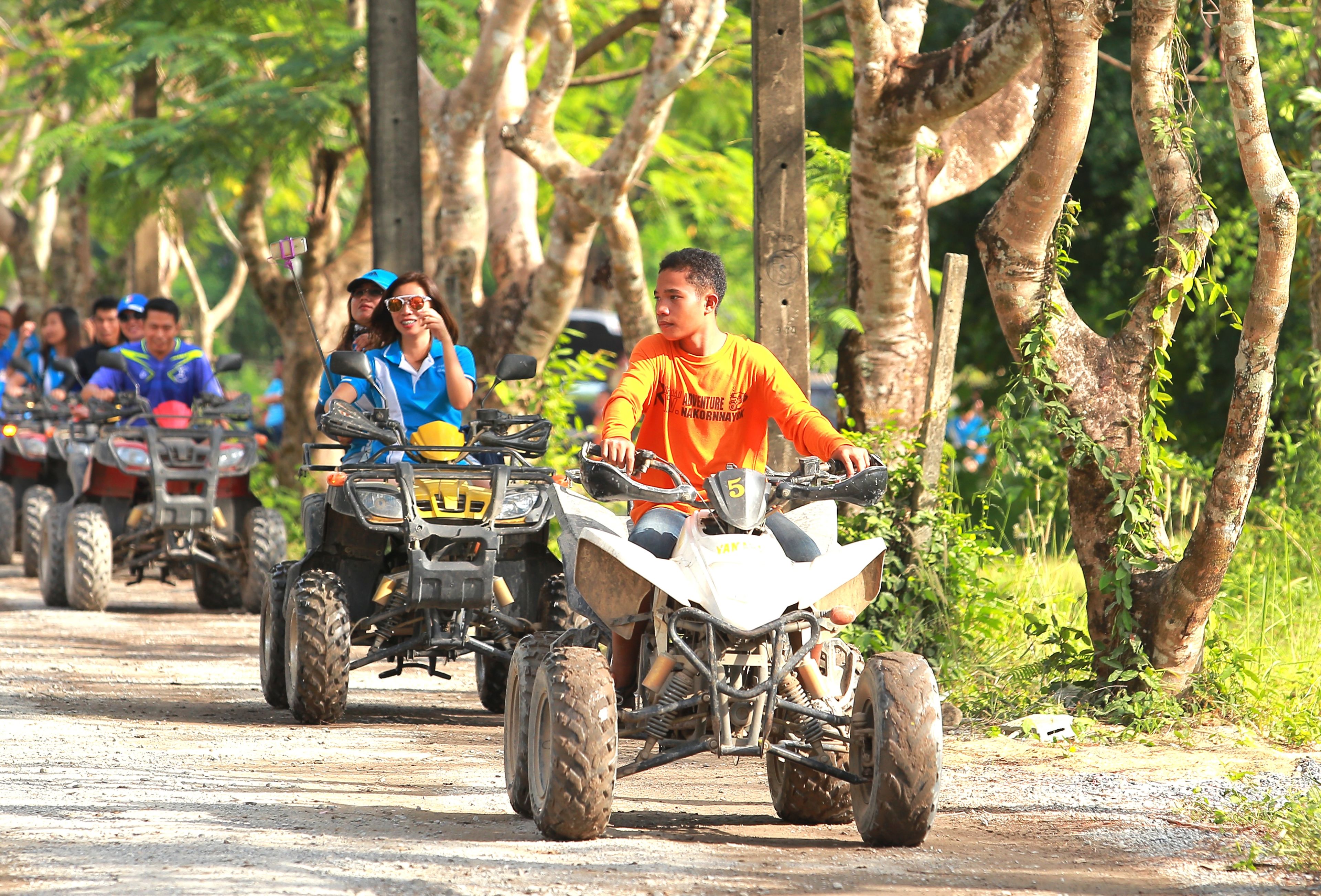 Group of people riding quad bikes through a scenic, tree-lined path during a fun outdoor adventure