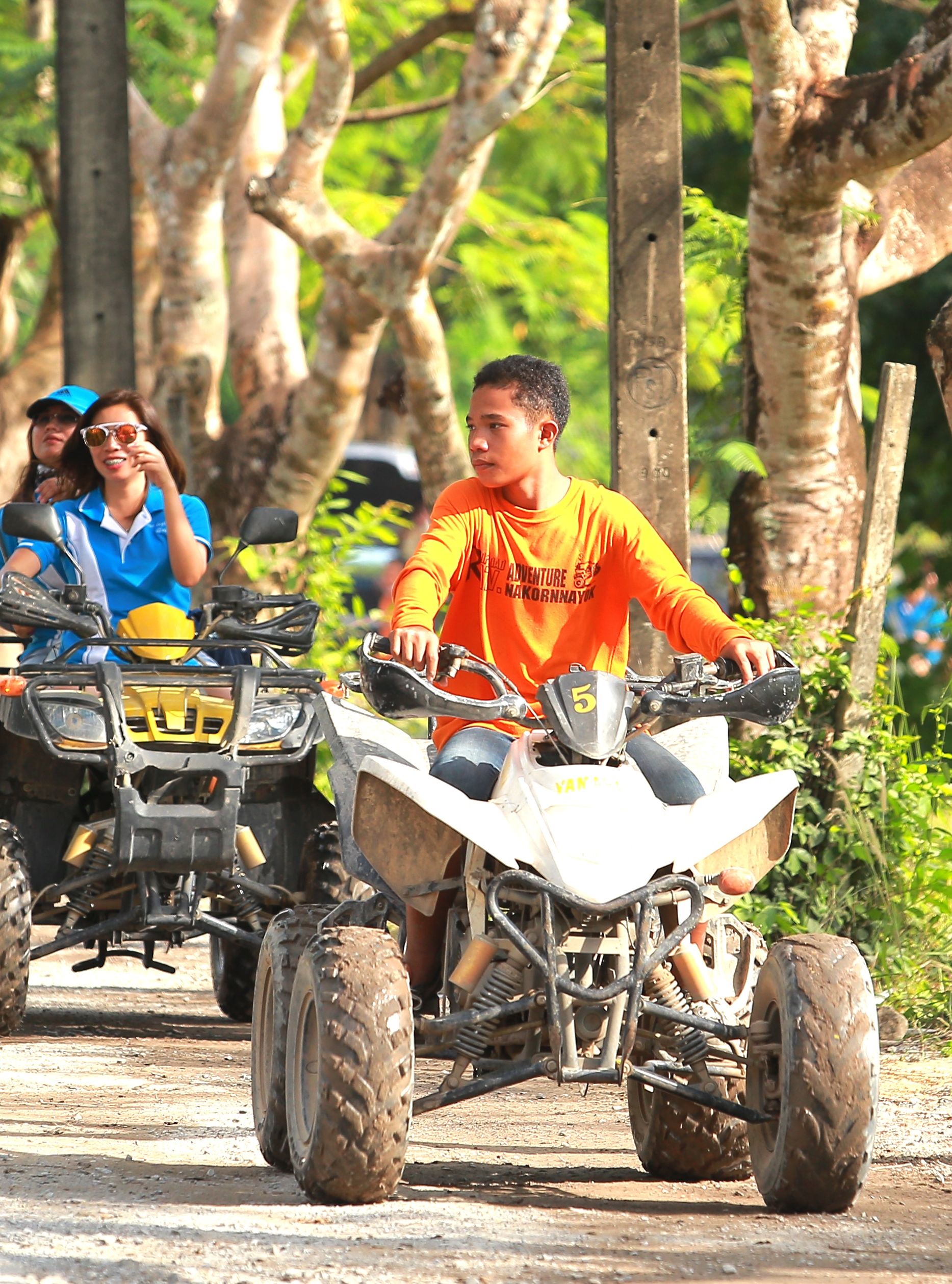 Group of people riding quad bikes through a scenic, tree-lined path during a fun outdoor adventure