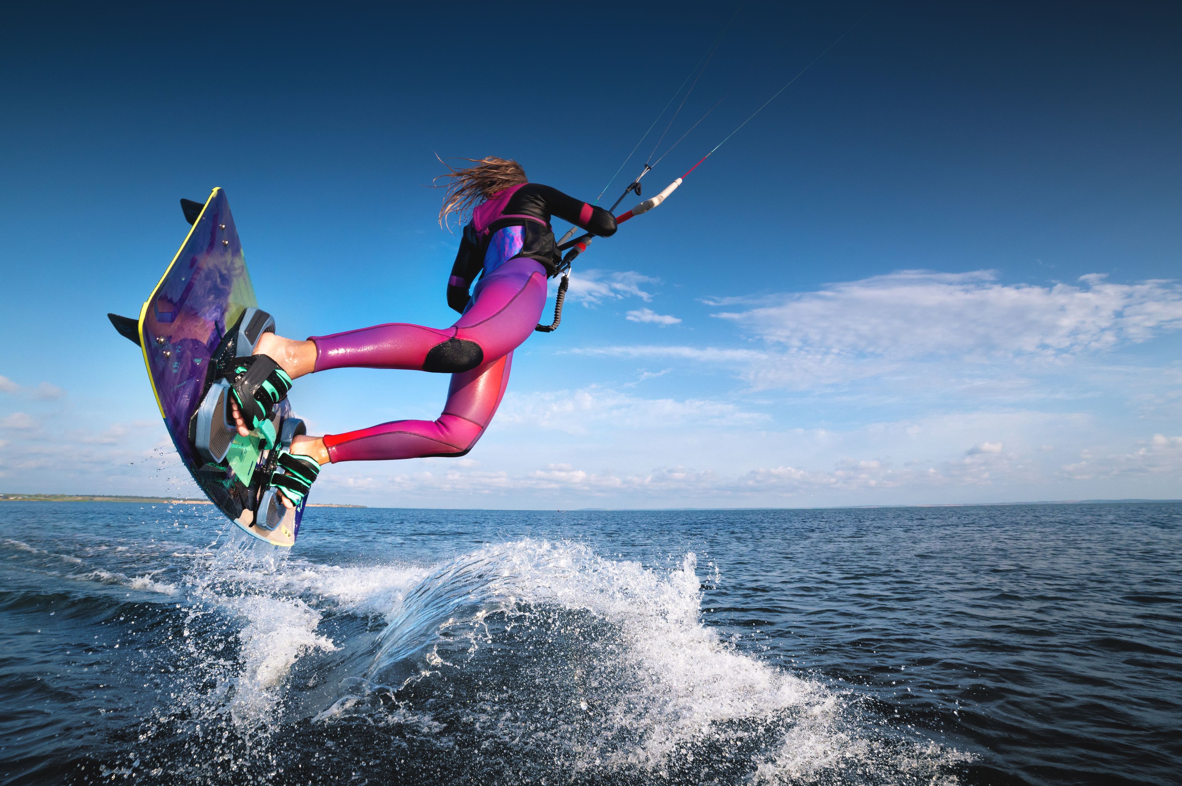 Kitesurfer mid-jump over water, with a bright sky in the background