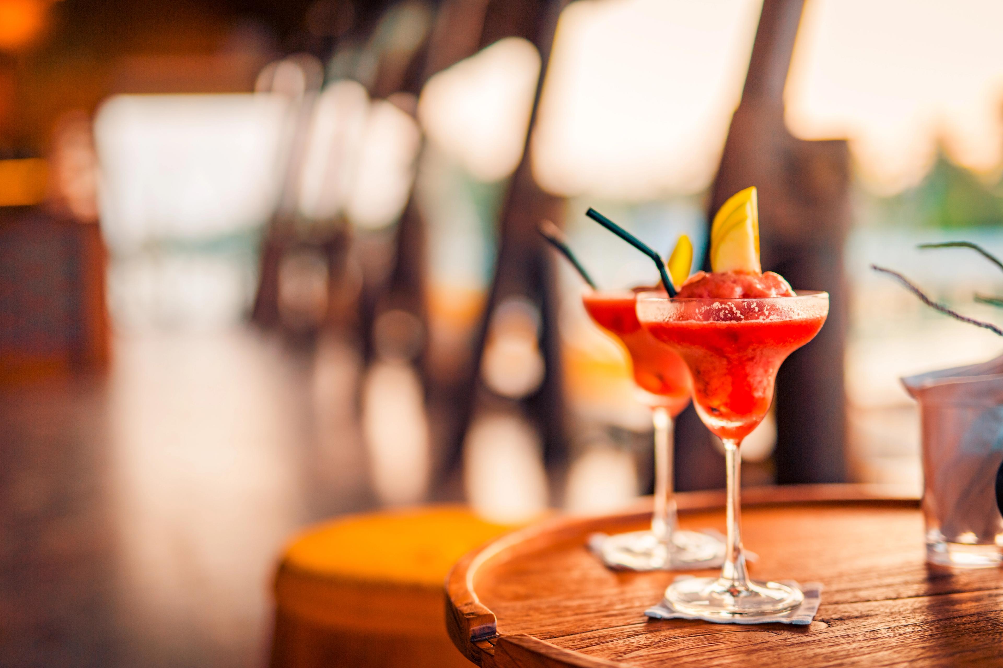 Two fruity cocktails with pineapple garnishes served on a wooden table, set against a warm, relaxing indoor ambiance