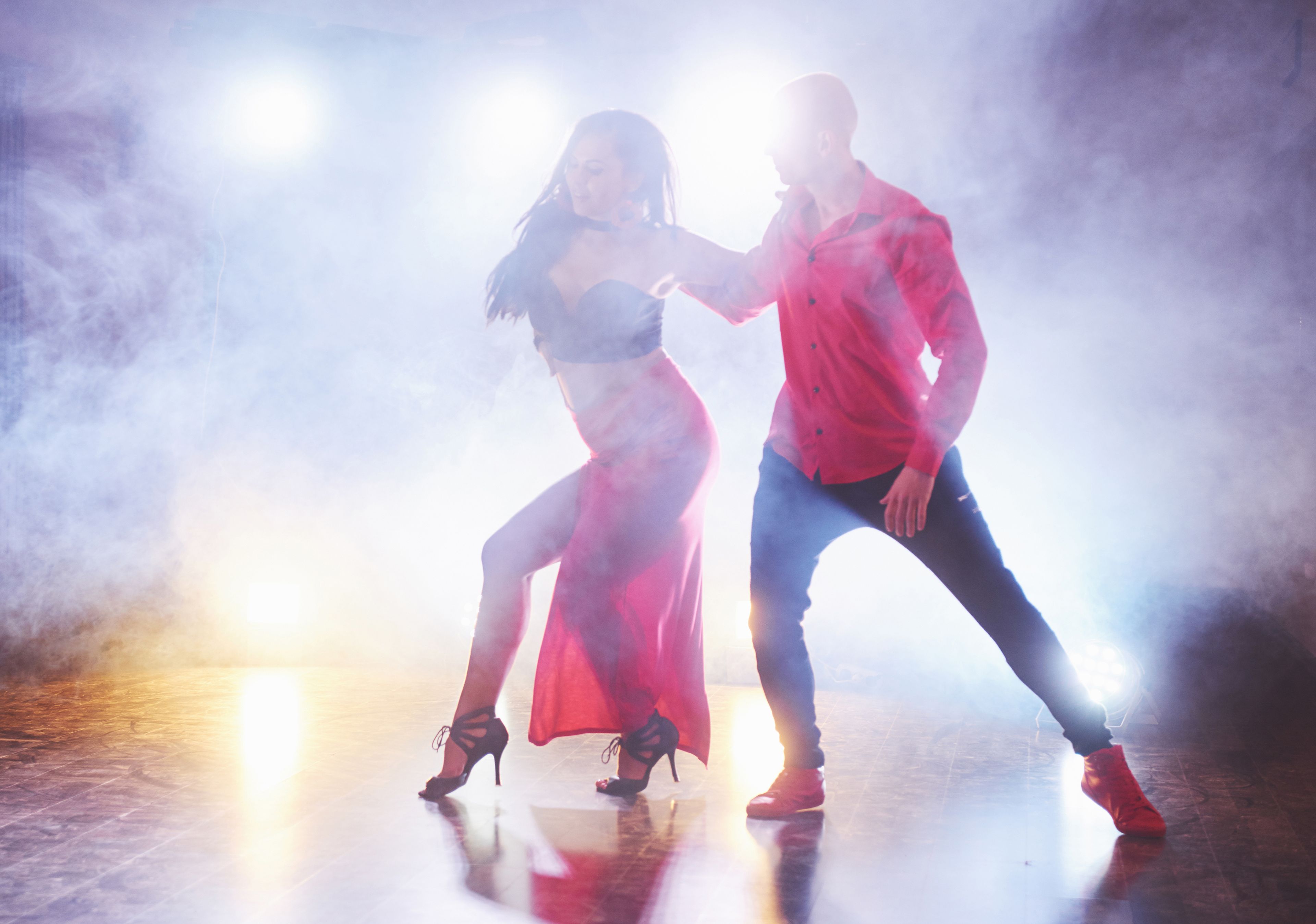 Two dancers performing under dramatic stage lighting, with mist adding to the dynamic atmosphere of the scene