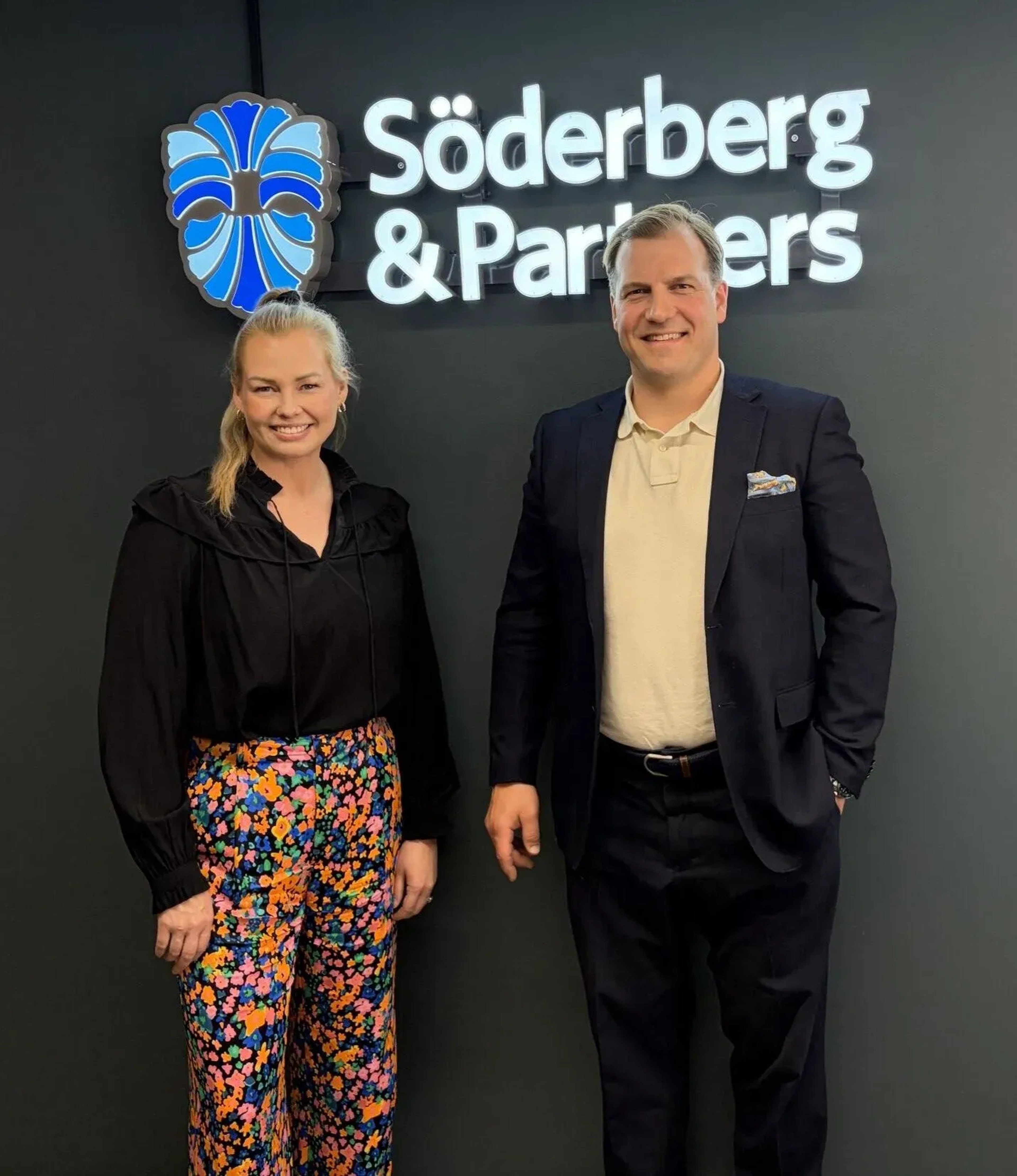 Söderberg & Partners ekonomichef Anu Suomilammi och Finadeck Oy:s vd Saku Pöllänen framför Söderberg & Partners logotyp