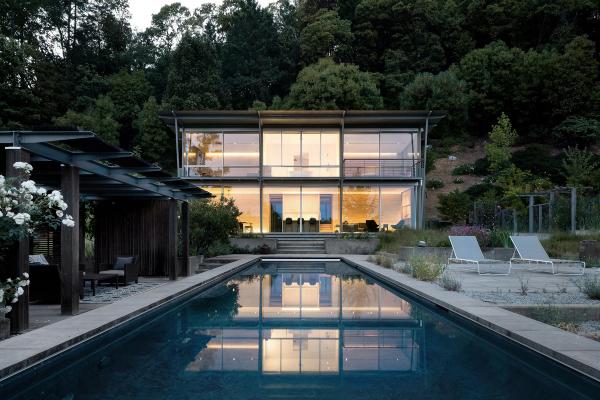 Modern glass home with a lap pool at dusk