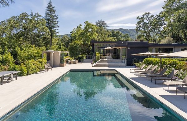 Long lap pool with a wide stone deck framed by oaks