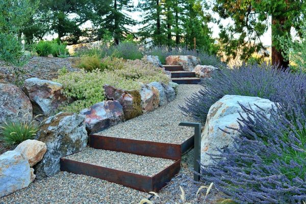 Corten steel steps through boulders and lavender on a hillside garden