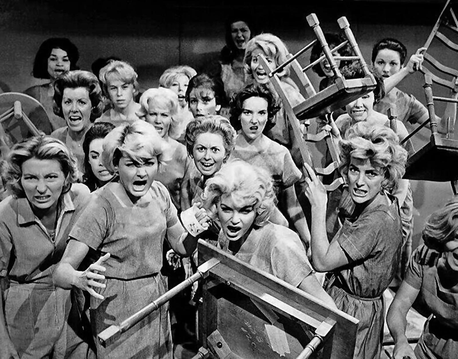 Black and white photograph showing a crowd of angry women wielding chairs and furniture as weapons in what appears to be a ri