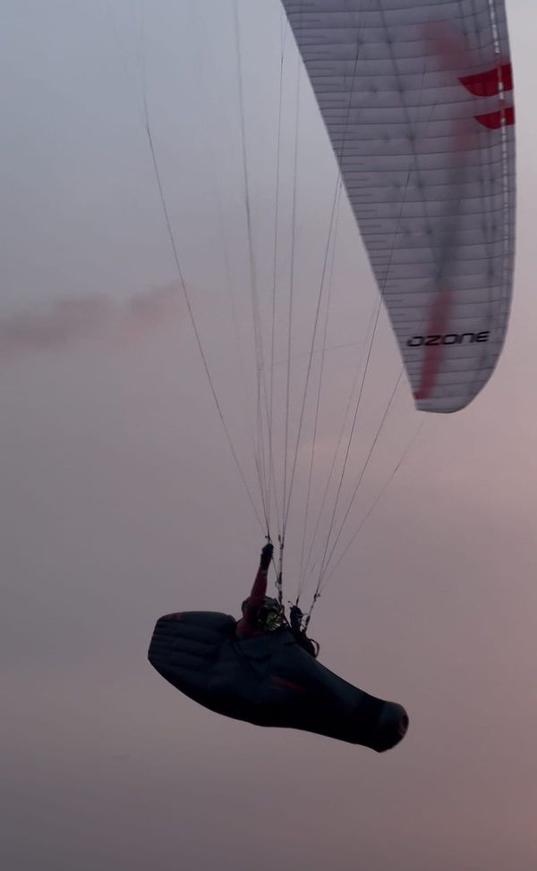 Pilot cruising in pod harness under Ozone wing at magic hour