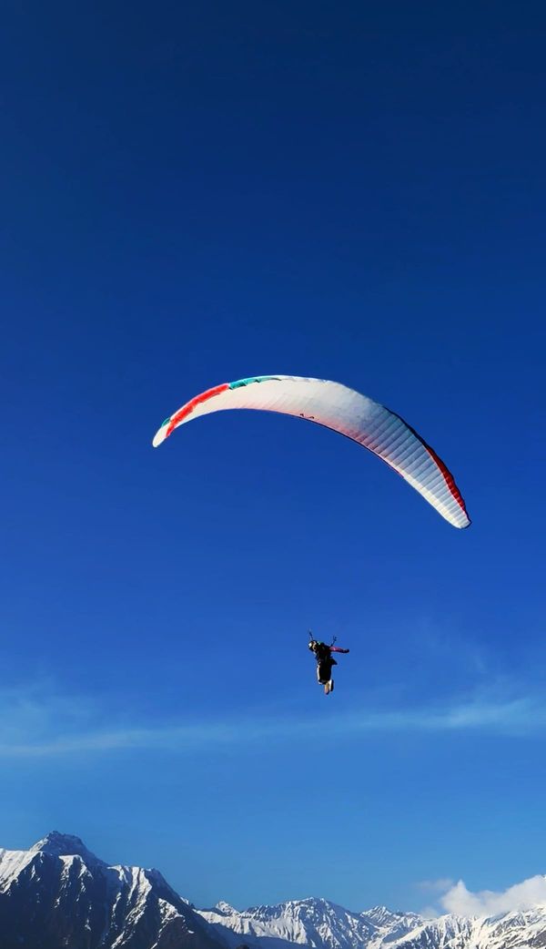 White paraglider against deep blue sky with snowy peaks below