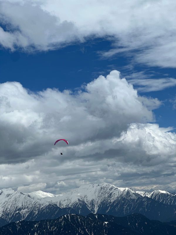 Pink paraglider above the Dhauladhar amid dramatic clouds