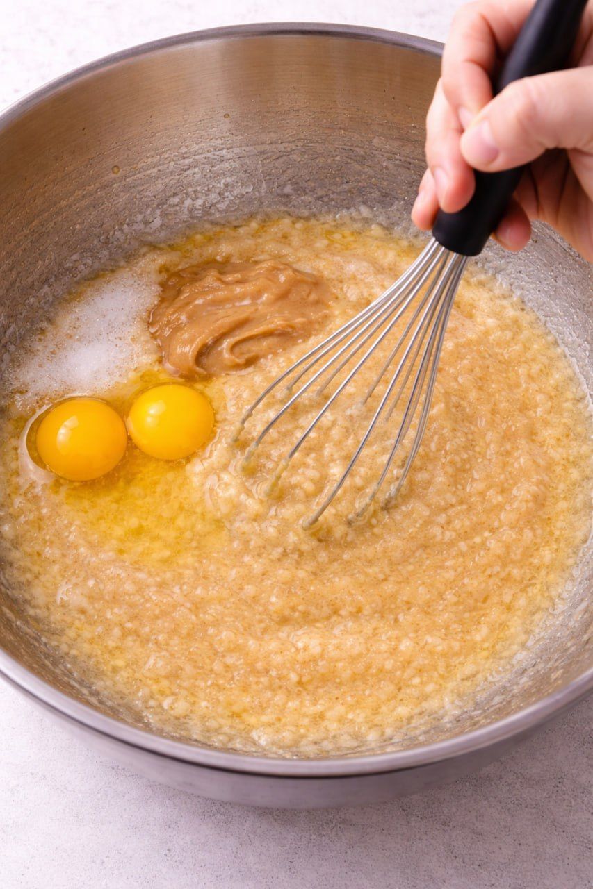 Whisking eggs, peanut butter, and sugar into mashed bananas.