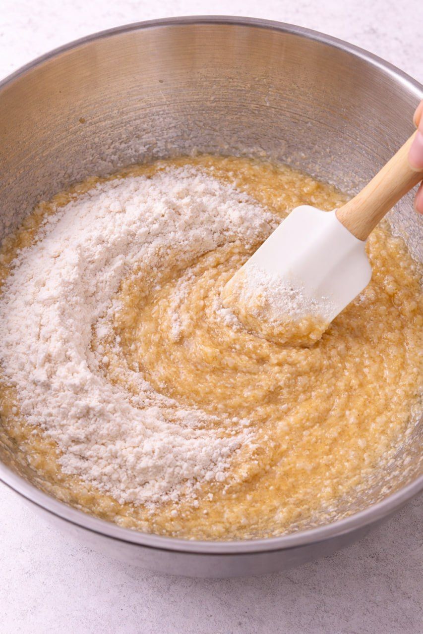 Folding flour into banana bread batter with a spatula.